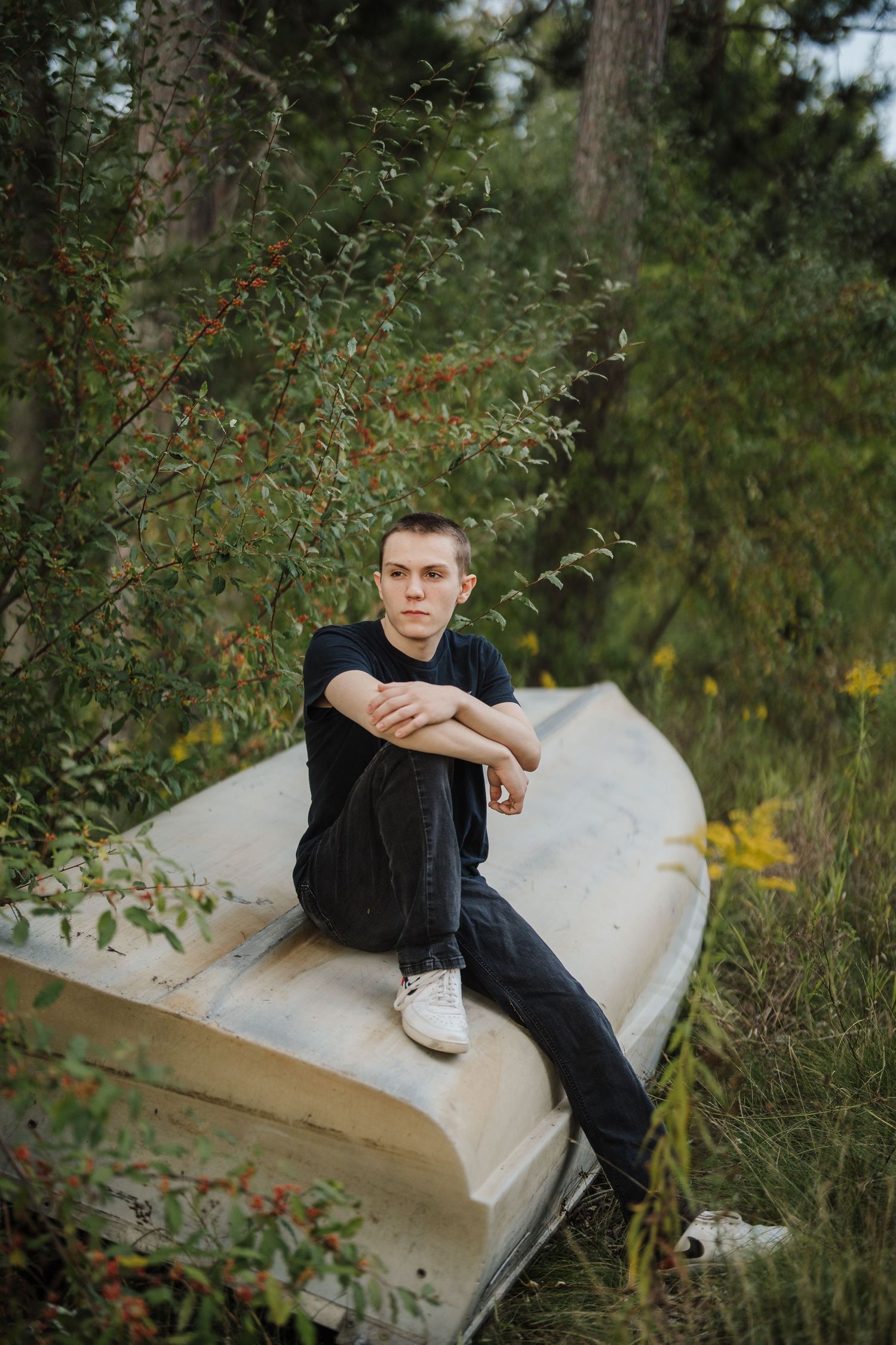 Person in dark jacket sits on white stone bench surrounded by lush greenery in outdoor setting.