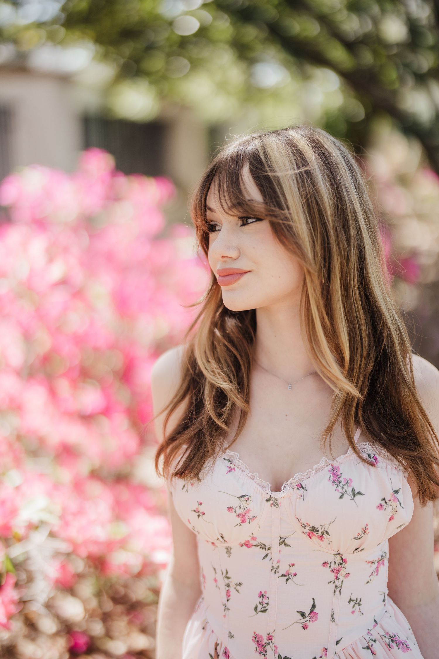 Romantic portrait session featuring a floral sundress against a backdrop of pink spring blossoms and greenery.