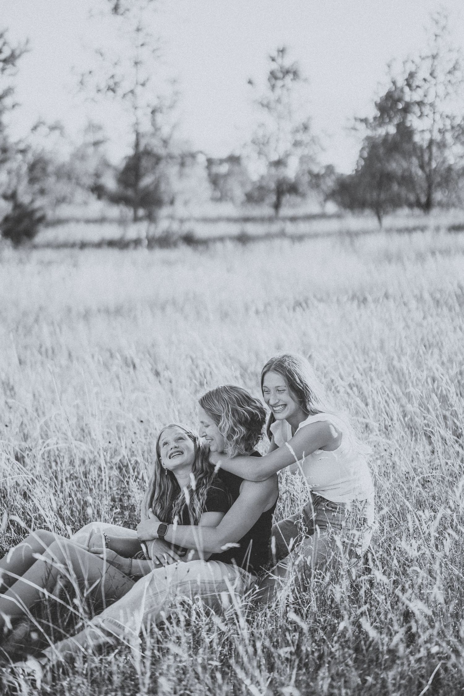 Two people laying in a field of tall grass and wildflowers, captured in black and white photography.