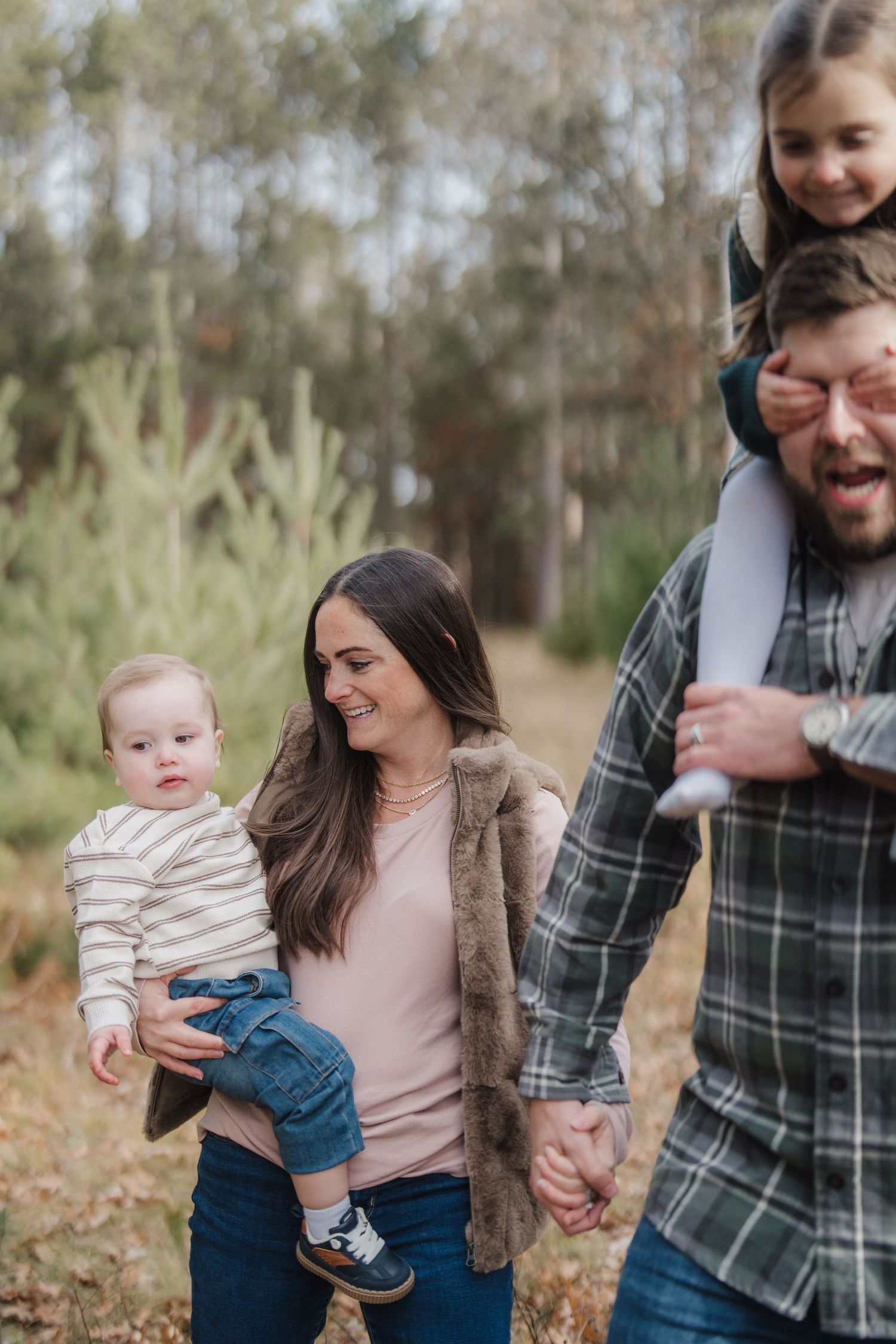 A candid family moment captured in a forest setting with natural lighting and fallen leaves.