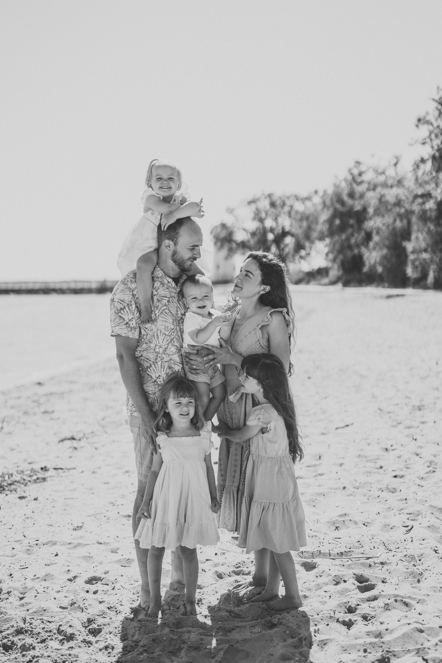 A family shares a joyful moment together on a sunny beach in black and white photography.