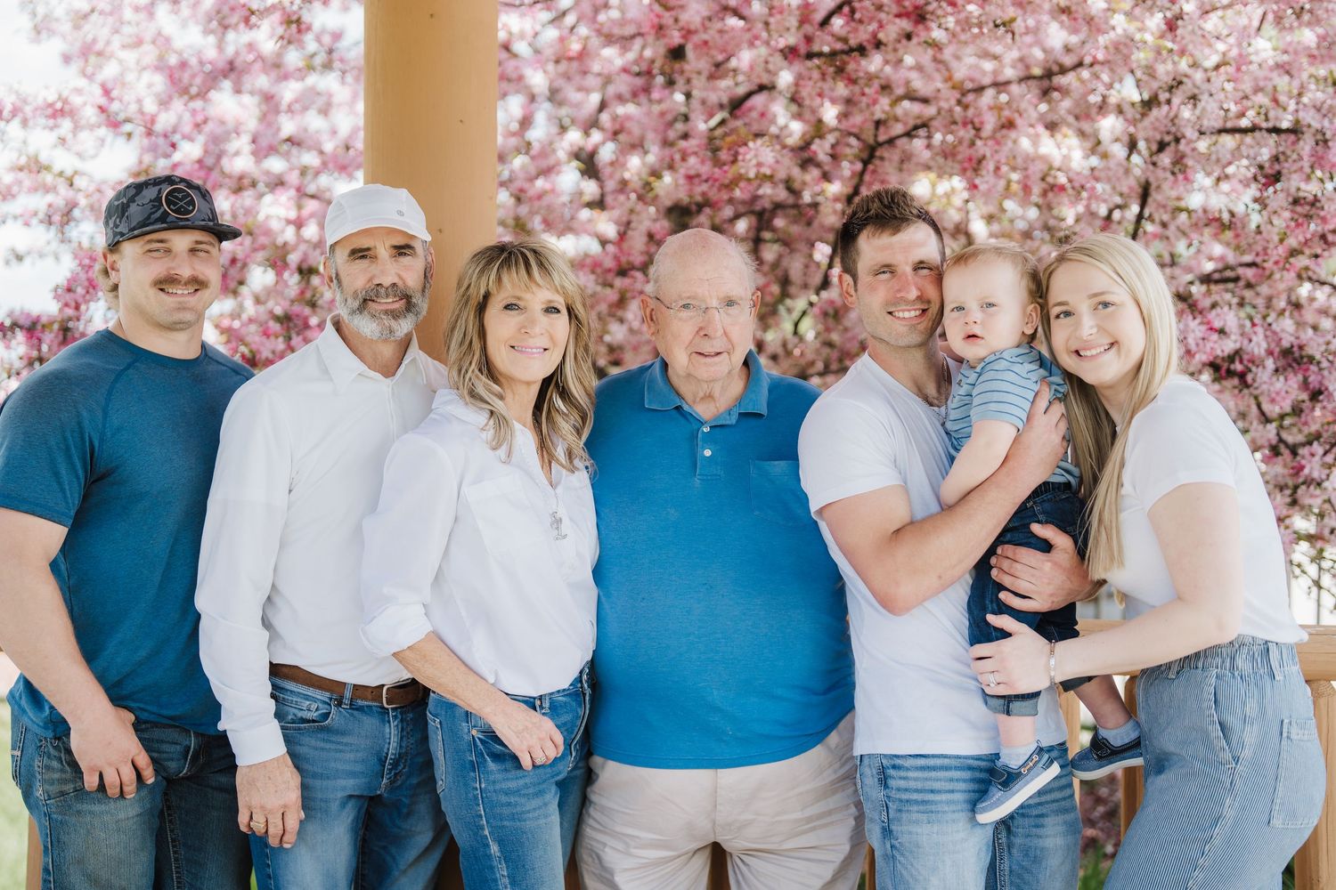 Family members pose together under blooming pink cherry blossom trees in coordinated blue and white outfits.