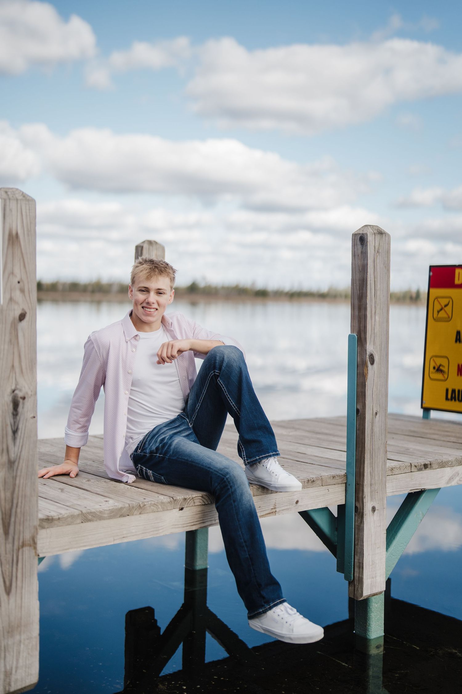 A person in casual attire lounges on a wooden dock over calm blue water on a cloudy day.