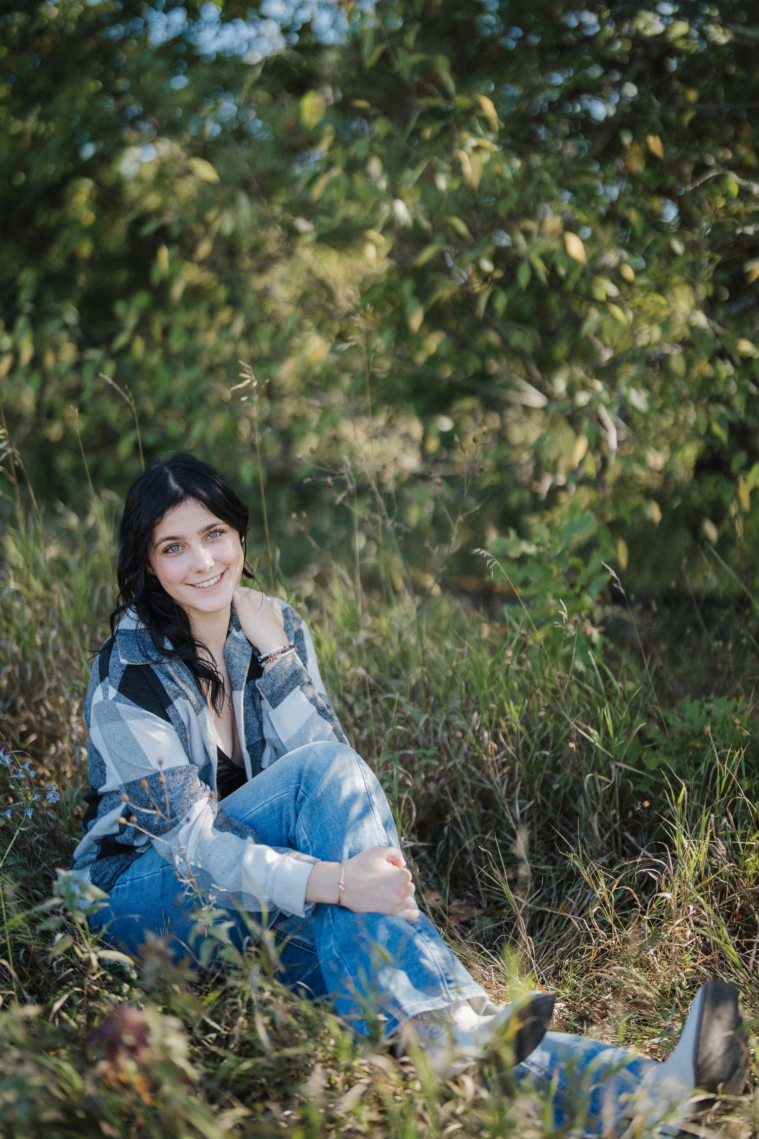 A casual portrait in nature showing someone wearing denim against lush green foliage.