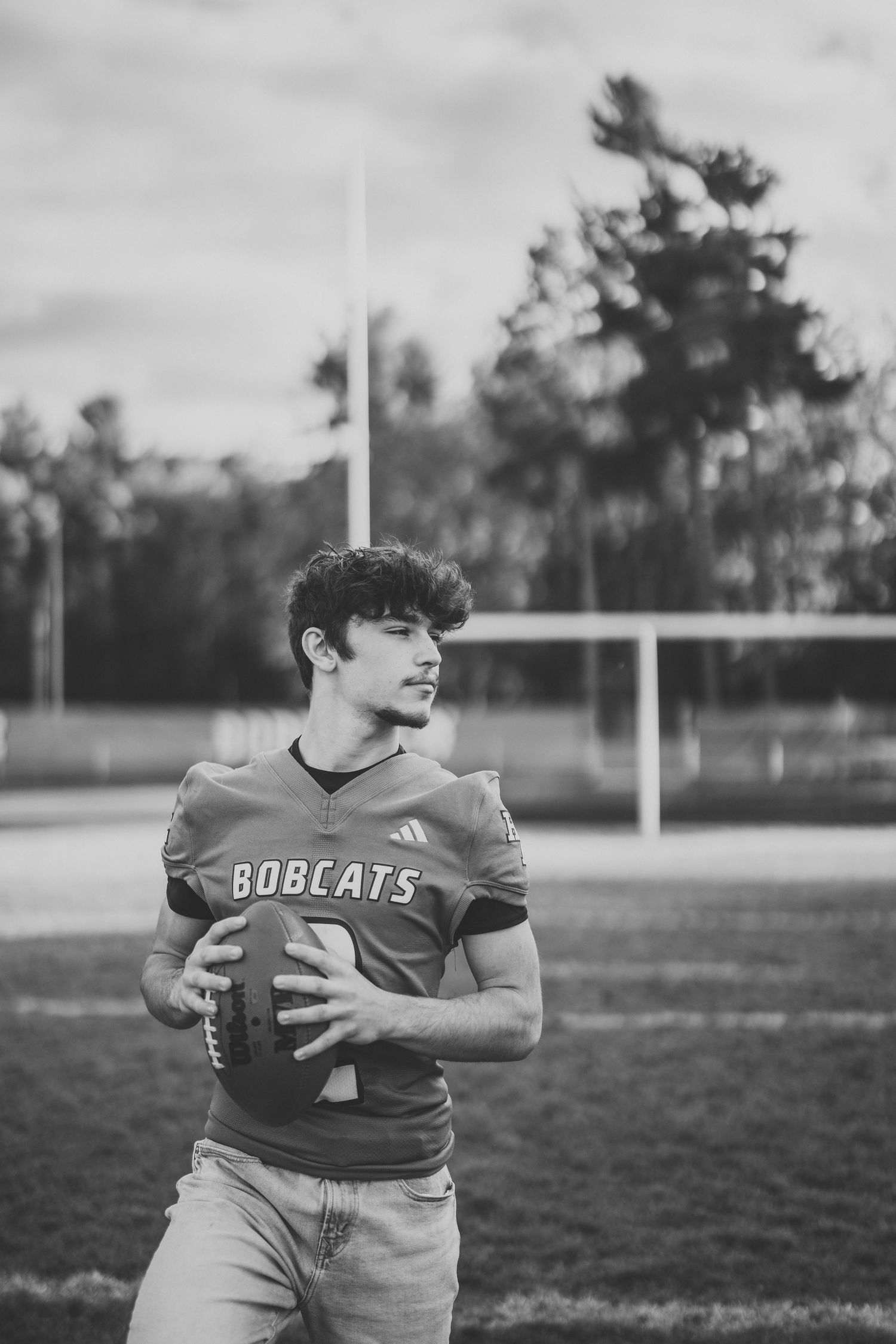 A young football player in a Bobcats jersey carries the ball across the field in a black and white photograph.
