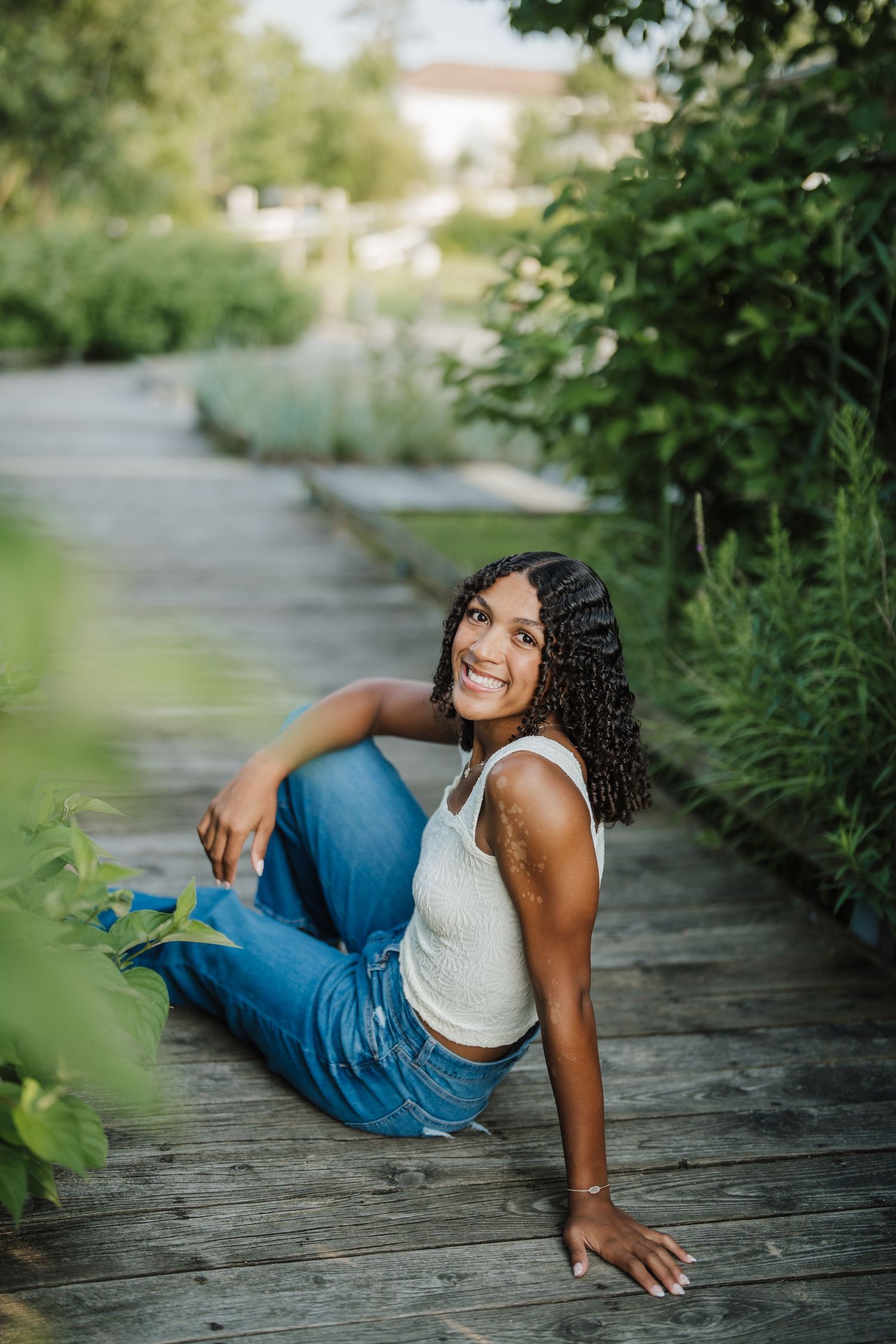 A series of outdoor portraits showing someone in a white top and jeans reclining on a wooden boardwalk surrounded by greenery.