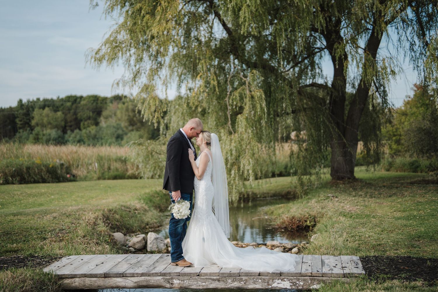 A couple shares a romantic moment under a weeping willow tree during their outdoor wedding celebration.