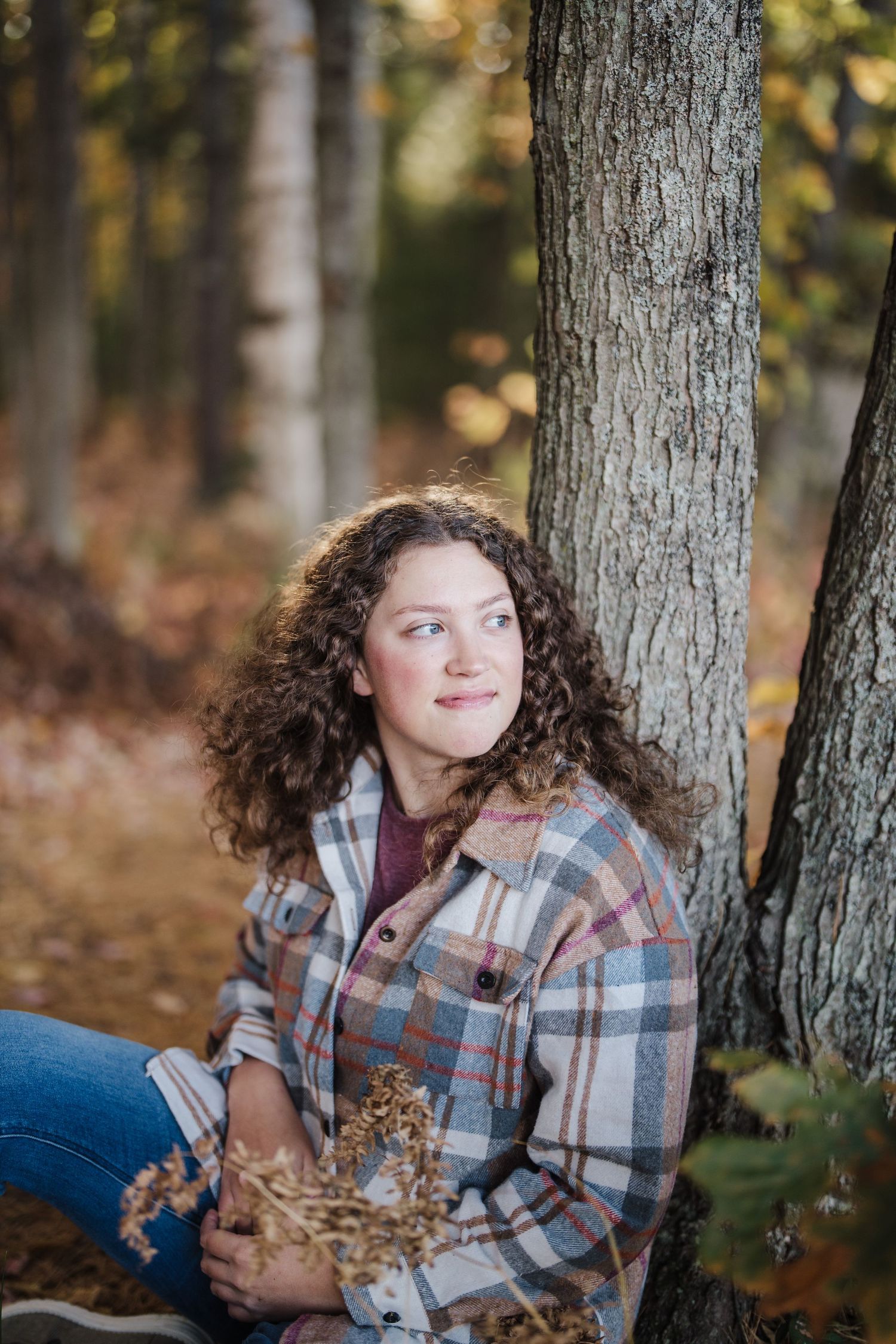 A series of outdoor portrait photos taken in autumn featuring someone in a plaid flannel jacket sitting against a tree trunk.