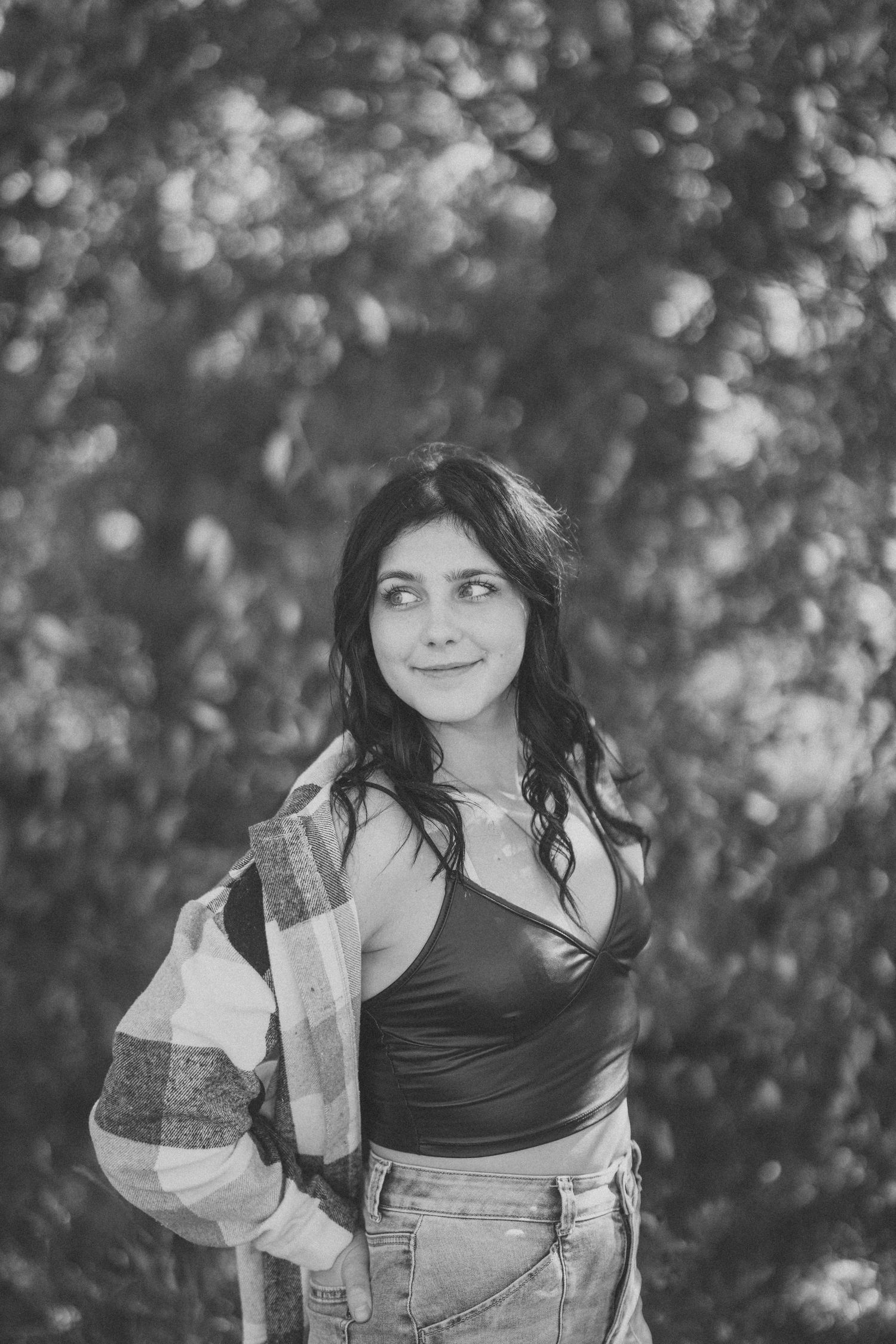 Black and white portrait of a person in overalls and black top against a blurred natural background.