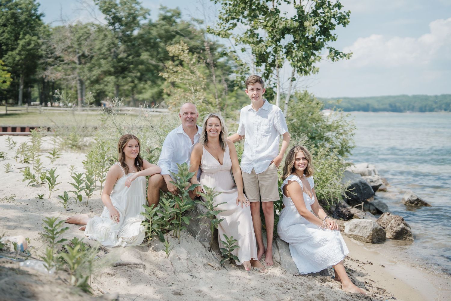 A series of romantic beachside photos showing people in white outfits sitting along a rocky shoreline on a sunny summer day.