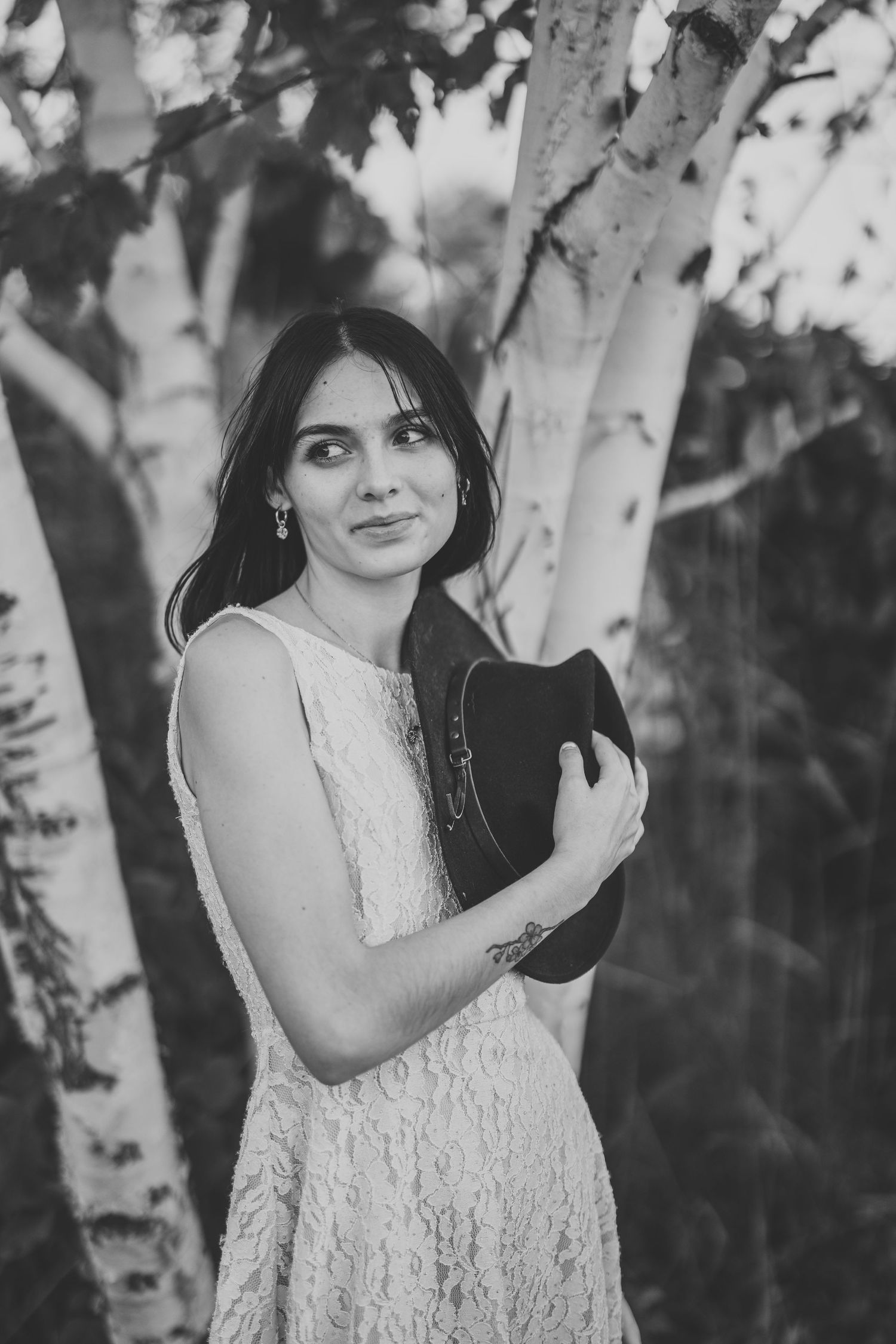 Black and white portrait series of a woman in a white lace dress posing near birch trees in a dreamy outdoor setting.
