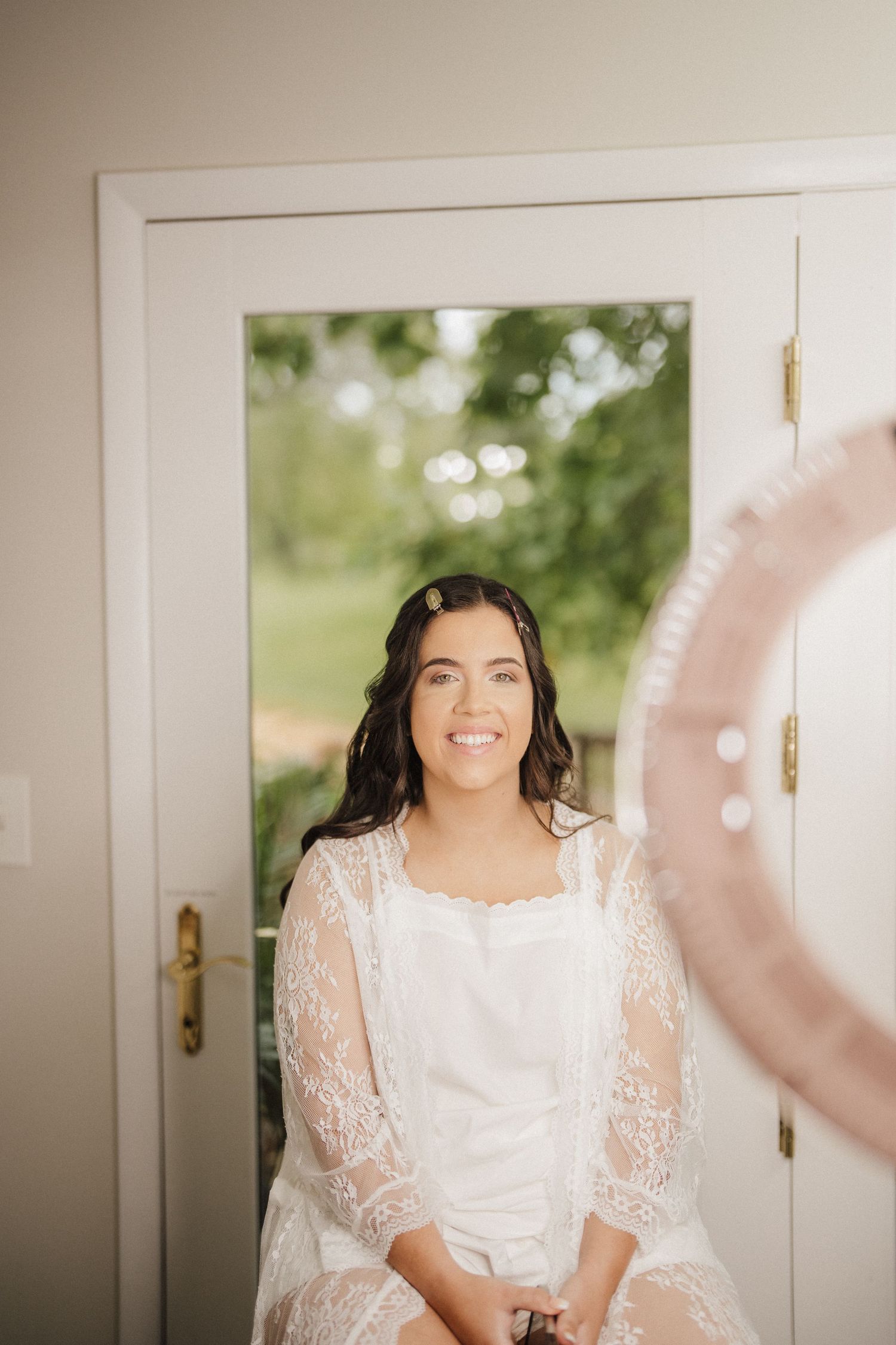 Bride in a delicate white lace dress getting ready on her wedding day with soft natural lighting.