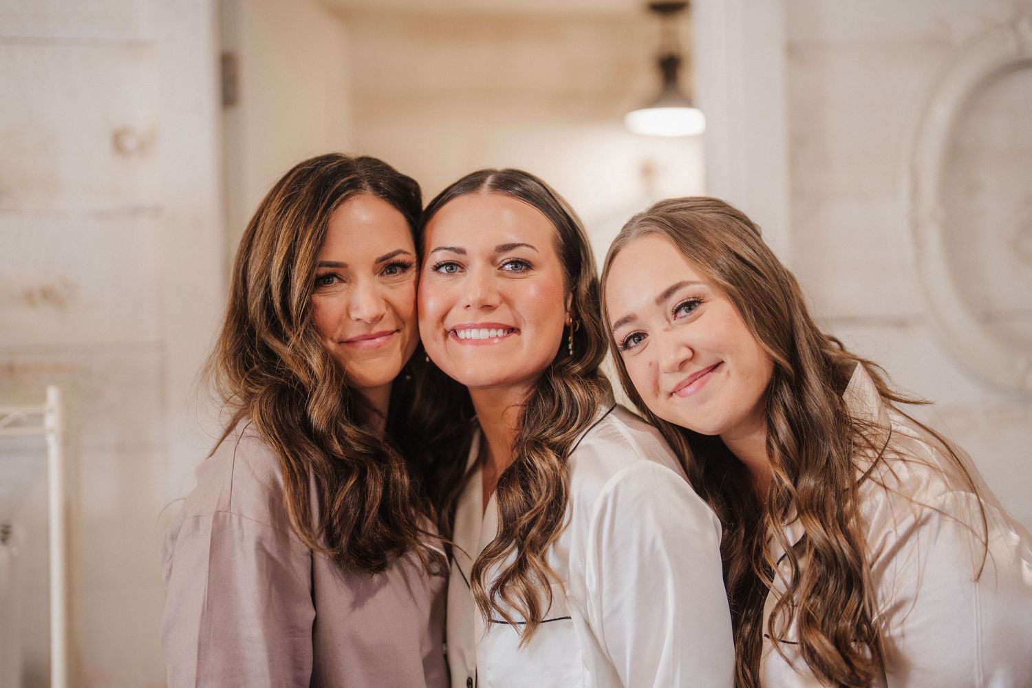 Three women smiling and laughing together in a bright white room during a joyful moment.
