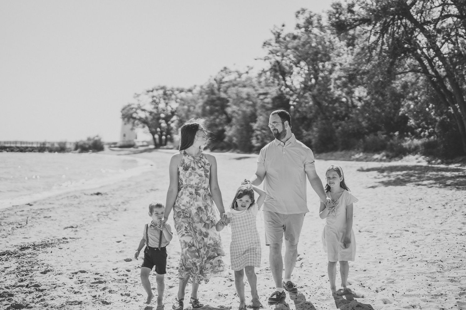Family wearing white and denim outfits walks together on a beach during sunset creating a silhouette effect.