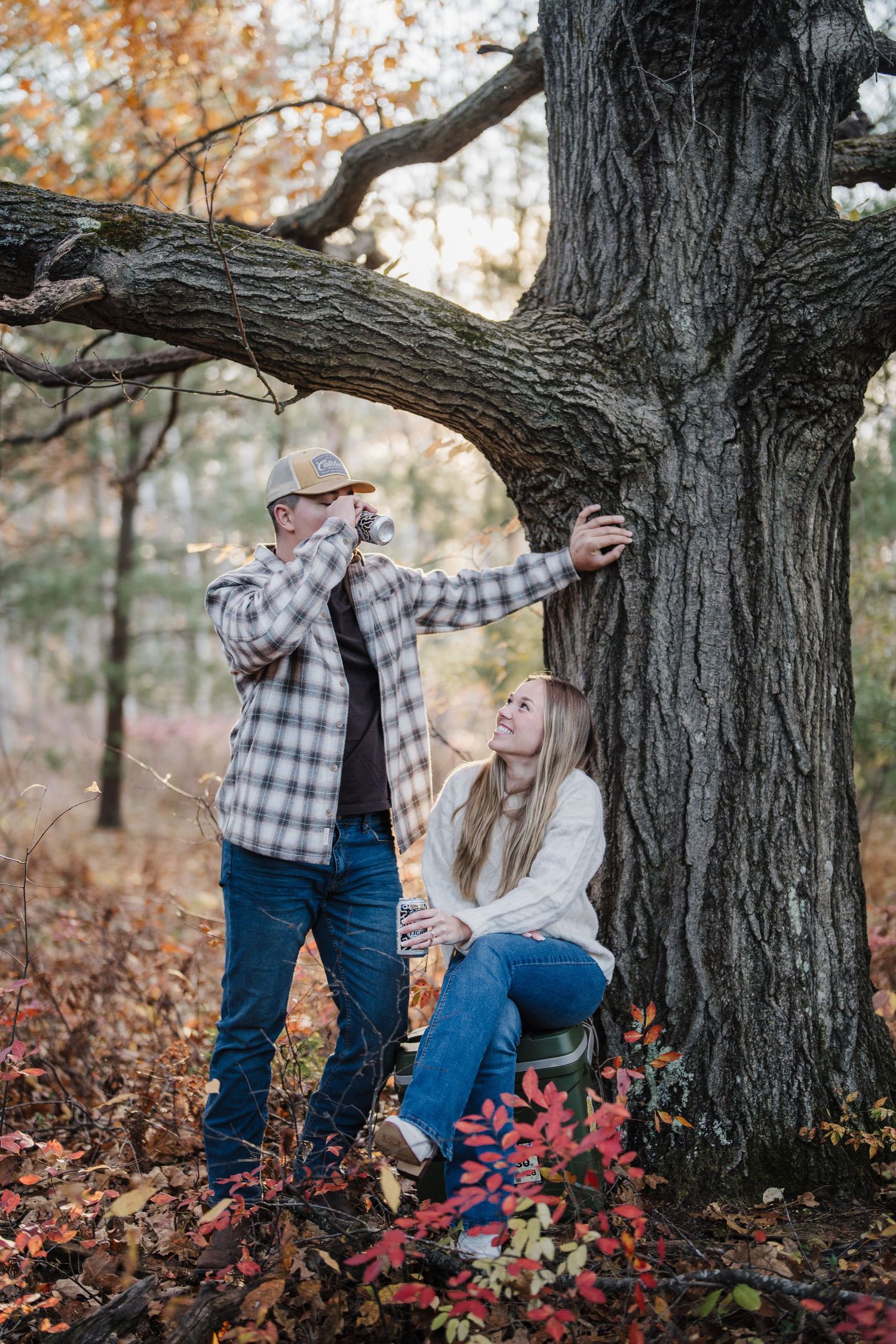 A romantic autumn photoshoot by a large tree trunk with fallen leaves in a forest setting.