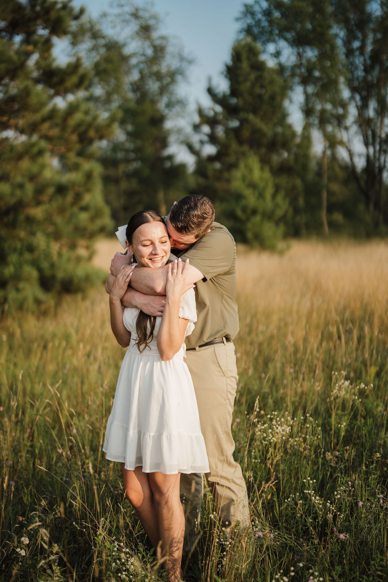 A couple embraces tenderly in a golden field of tall grass during sunset.