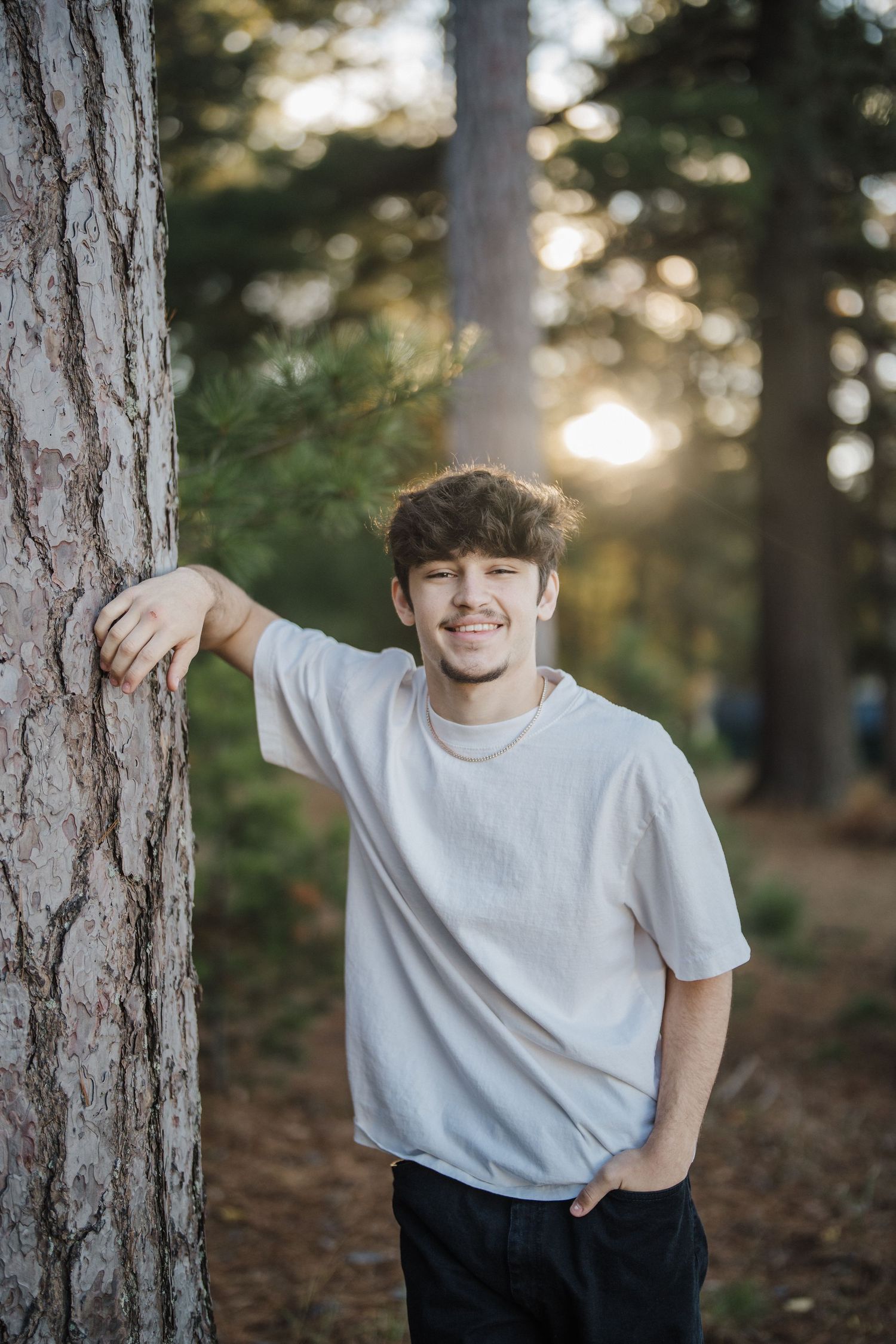 Casual portrait among pine trees during sunset in white t-shirt.
