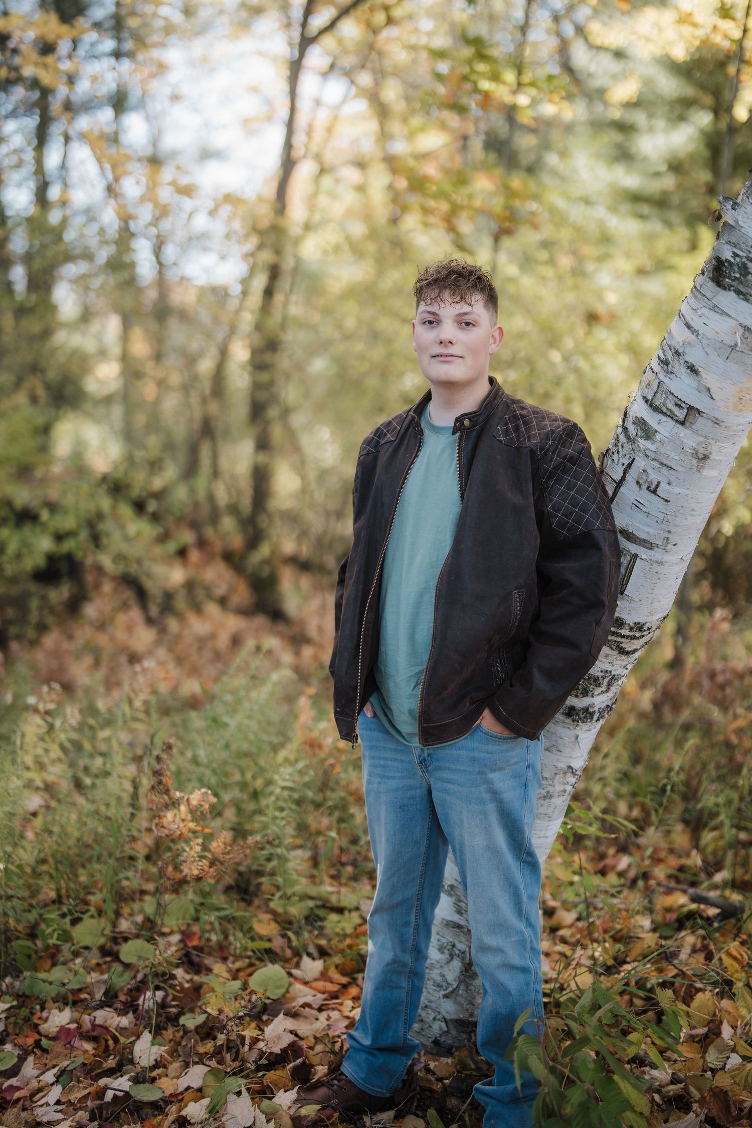 Autumn outdoor portrait session with birch trees and fallen leaves in a wooded setting.