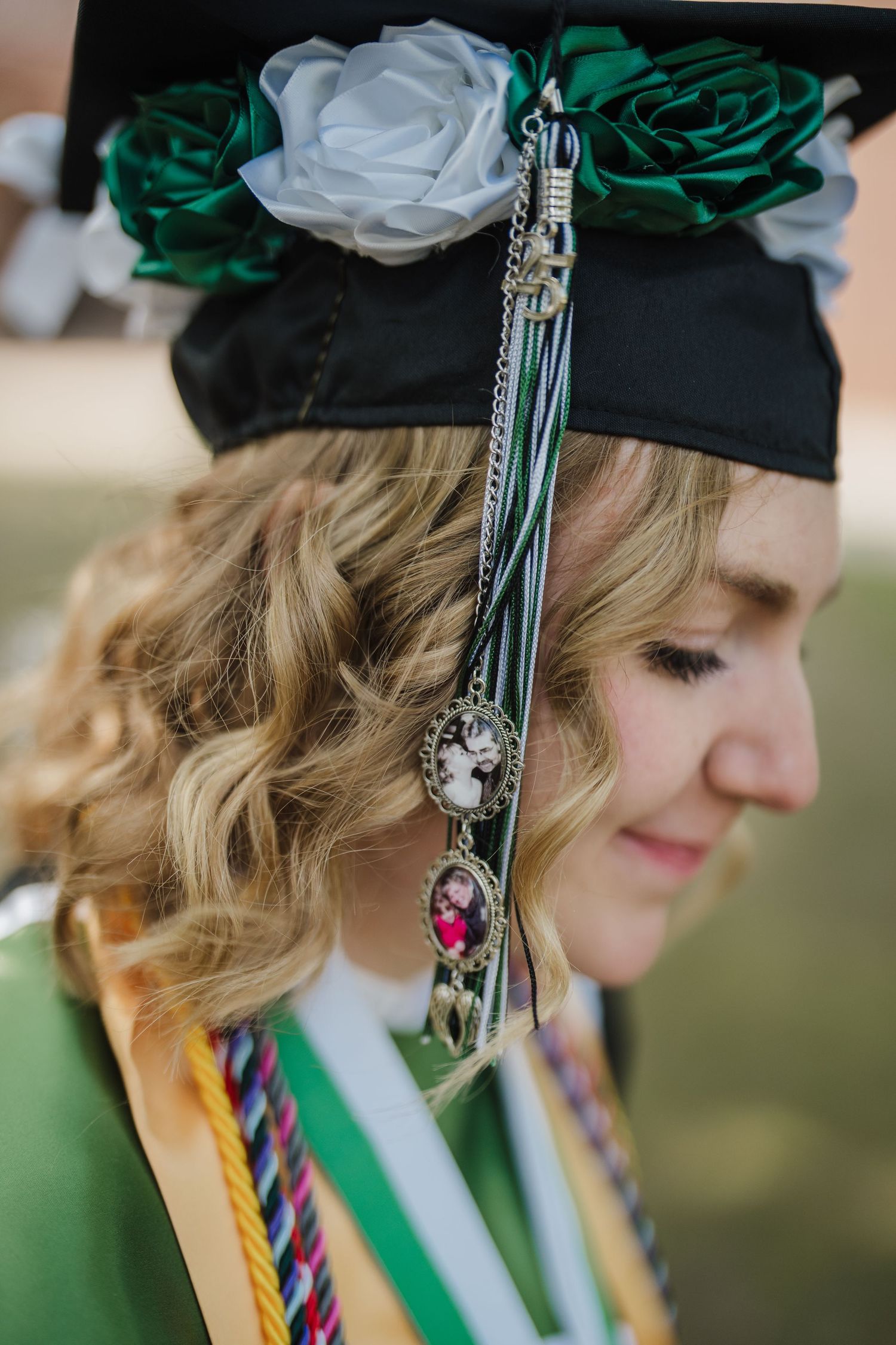 Graduation cap decorated with emerald green and white roses features dangling ornate tassels and charms.