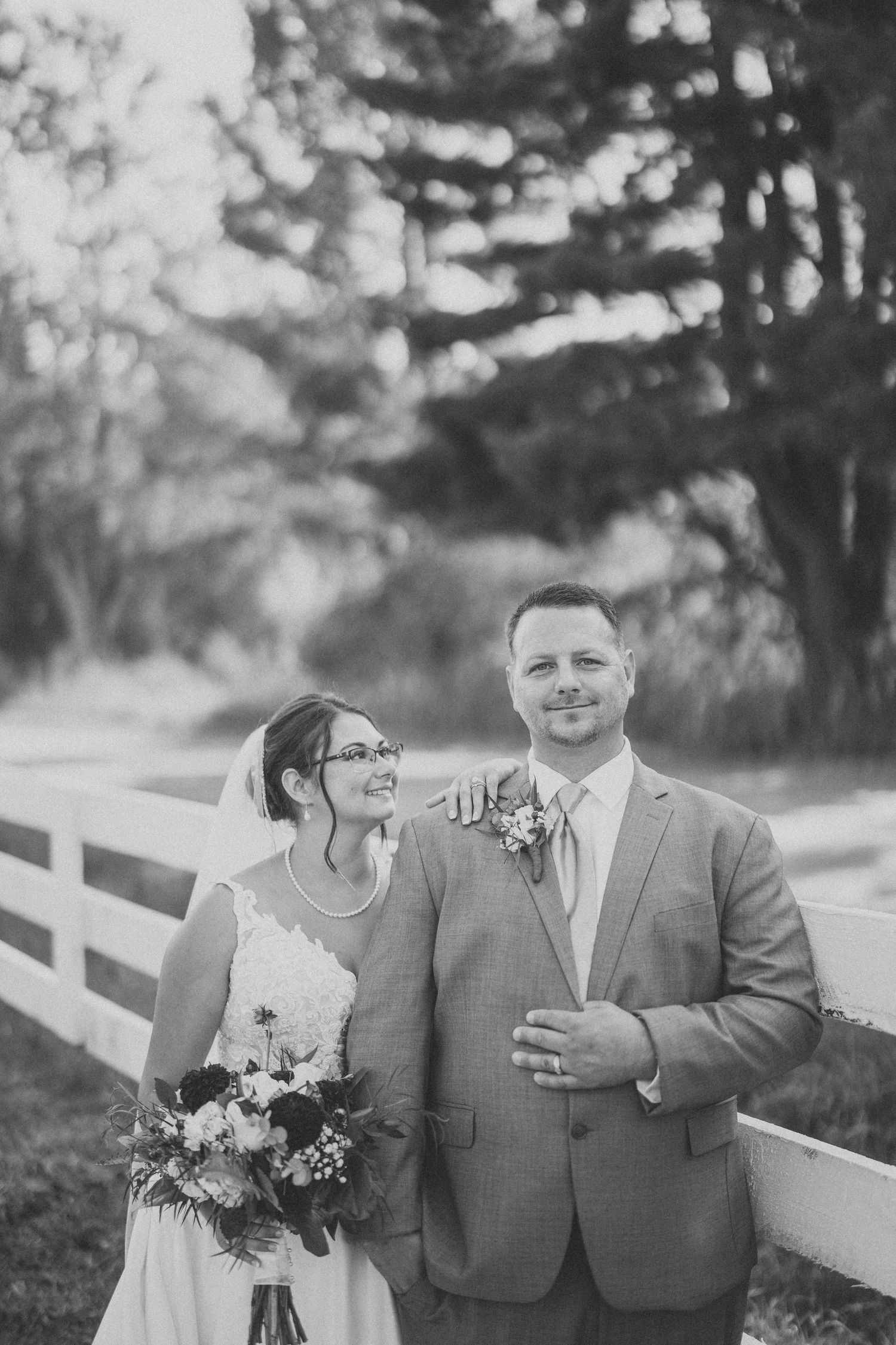 A couple shares a joyful moment together on their wedding day near a white fence.