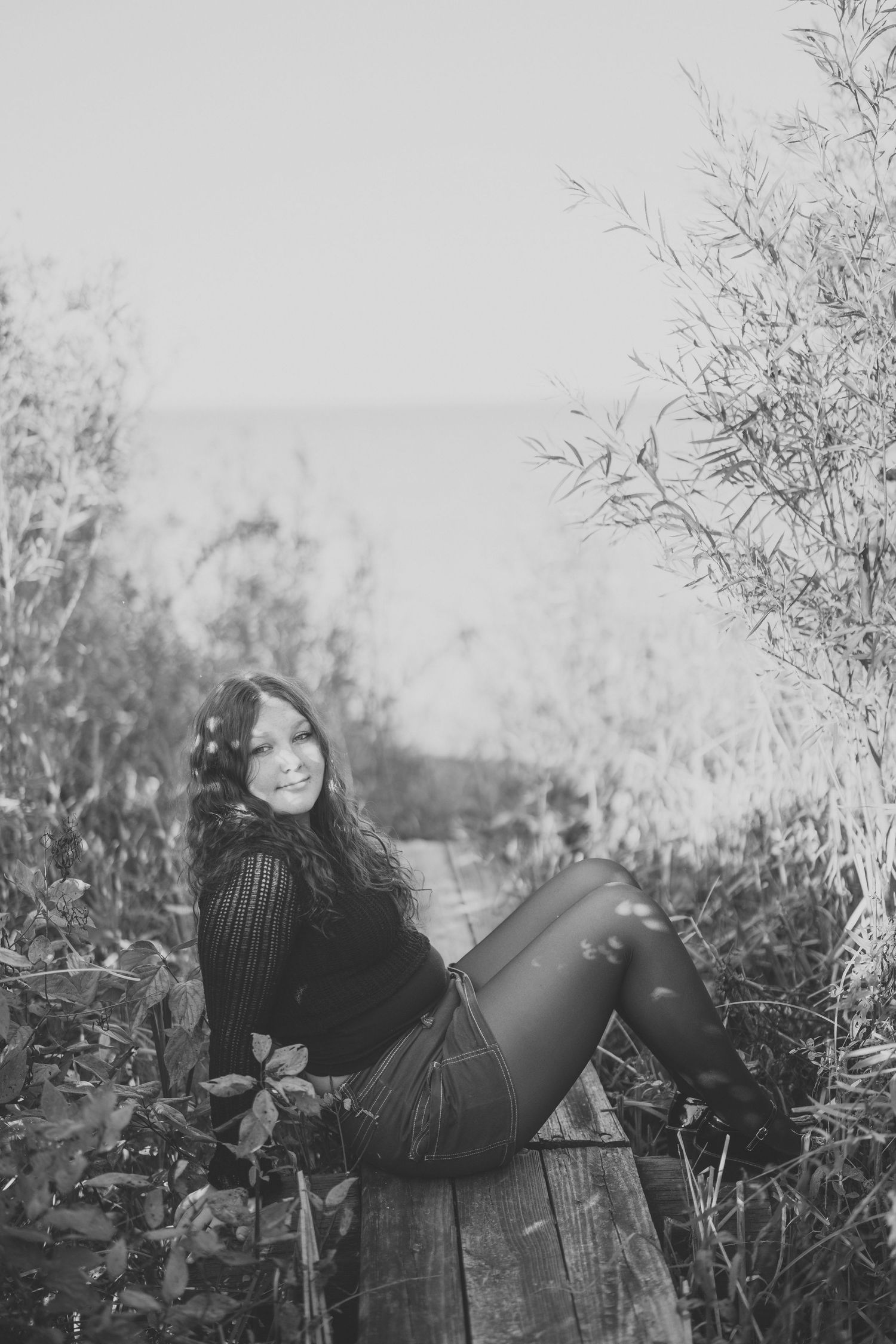 Black and white portrait on wooden platform surrounded by tall grasses and foliage.