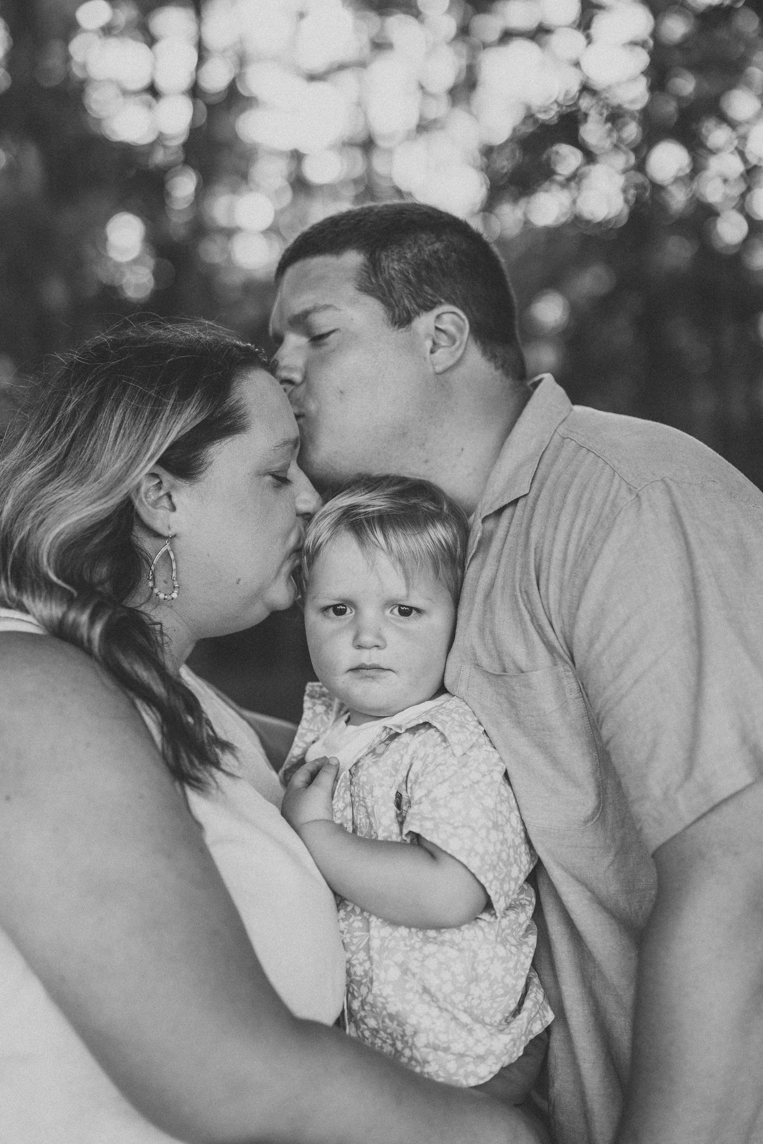 A series of black and white photos showing tender family moments between parents and a young child in outdoor lighting.