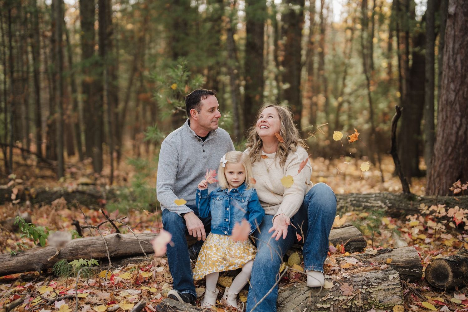 Couple sits together on fallen log in autumn forest during outdoor photoshoot.