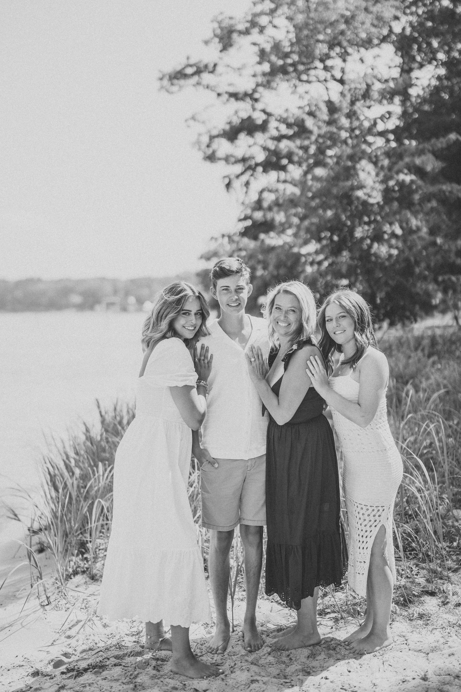 Group of friends enjoying a casual summer day together on a sandy beach with trees in the background.