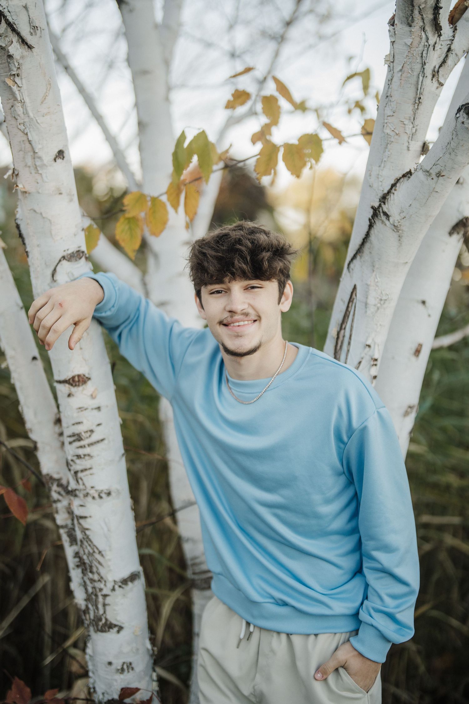 Casual portrait among birch trees with someone wearing light blue sweater in autumn setting.