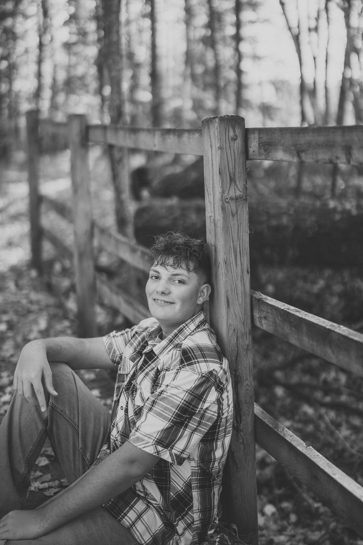 A black and white photo series shows someone in a plaid shirt reclining against a wooden fence in a forest setting.