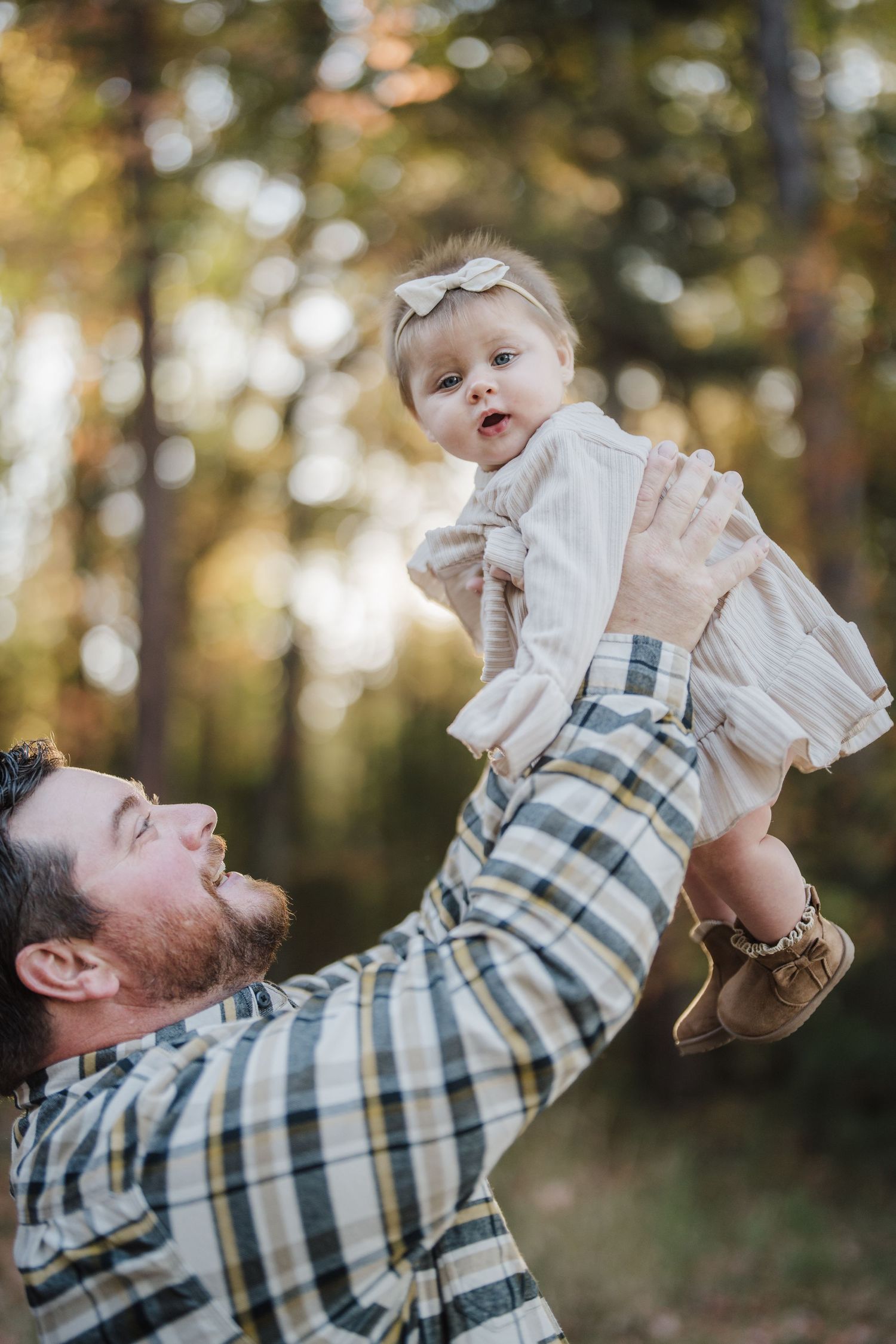 A person in a plaid shirt lifts a baby wearing white clothing in a series of joyful outdoor photos with autumn trees.