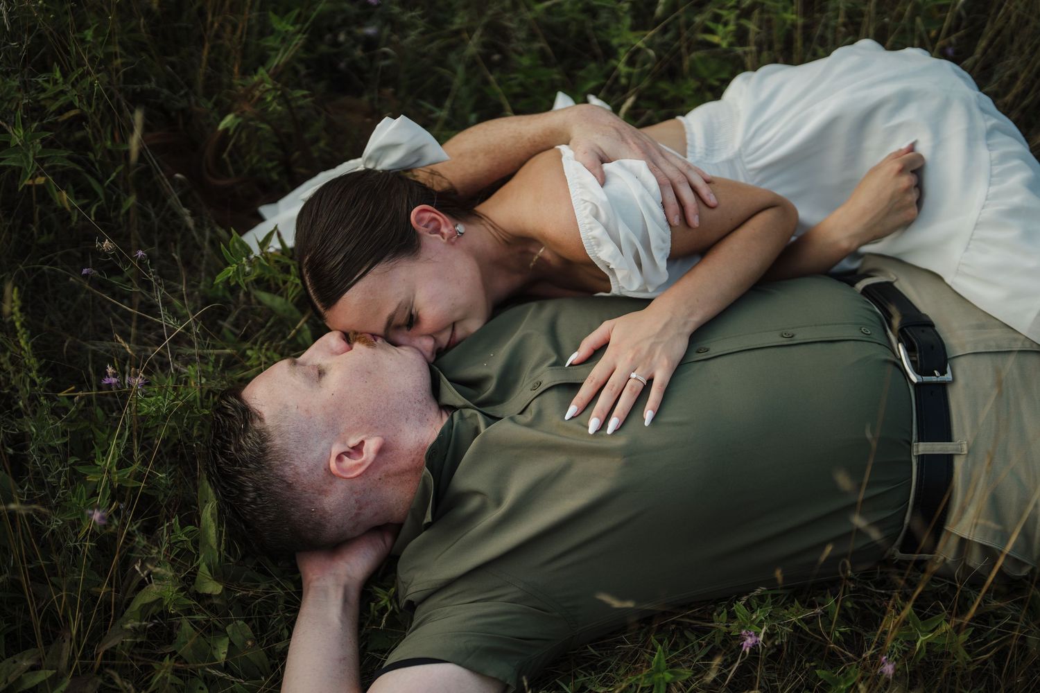 Two people laying in tall grass share an intimate moment together while wearing casual clothing.