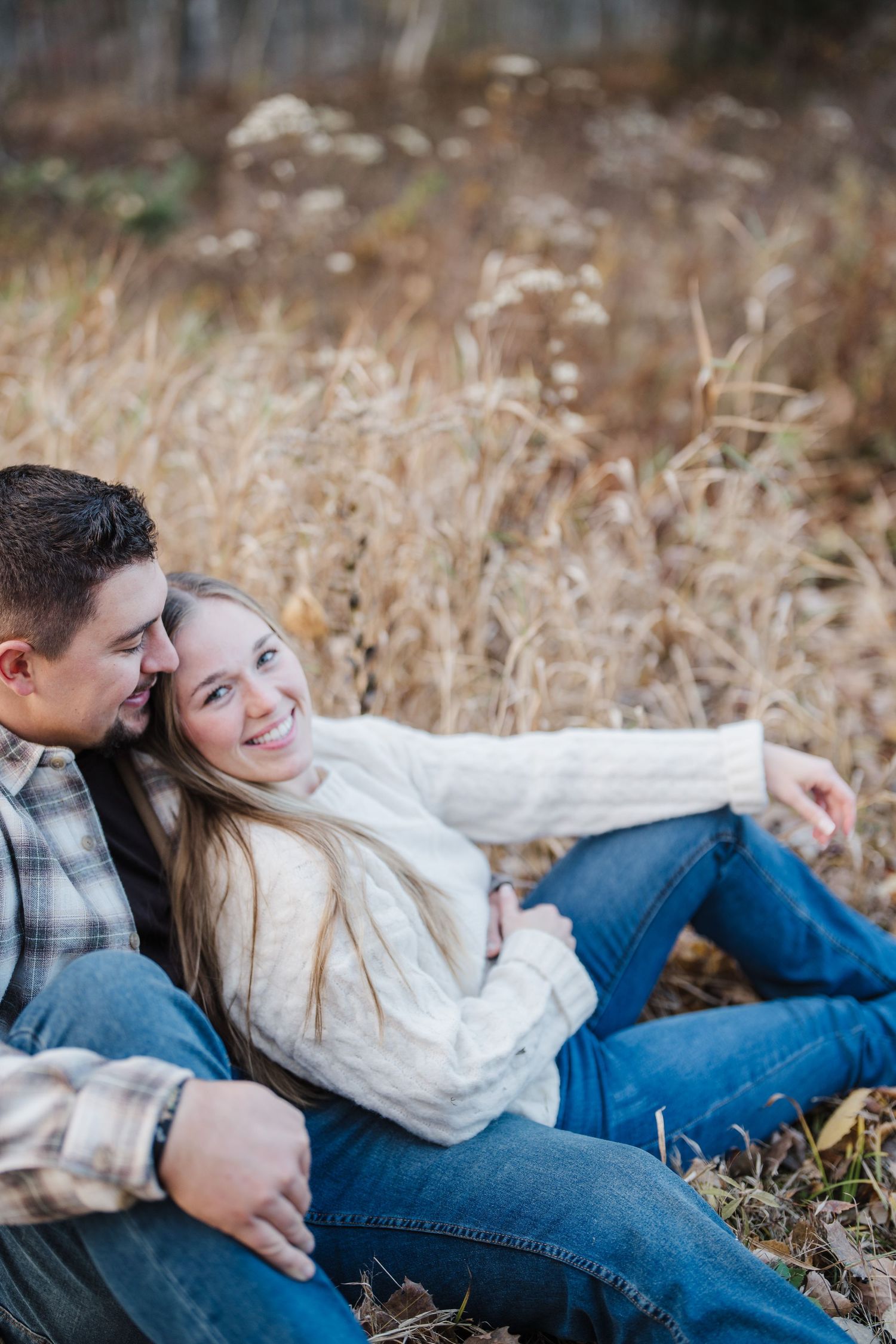 Couple relaxing together in a field of tall dried grass during an autumn photoshoot.