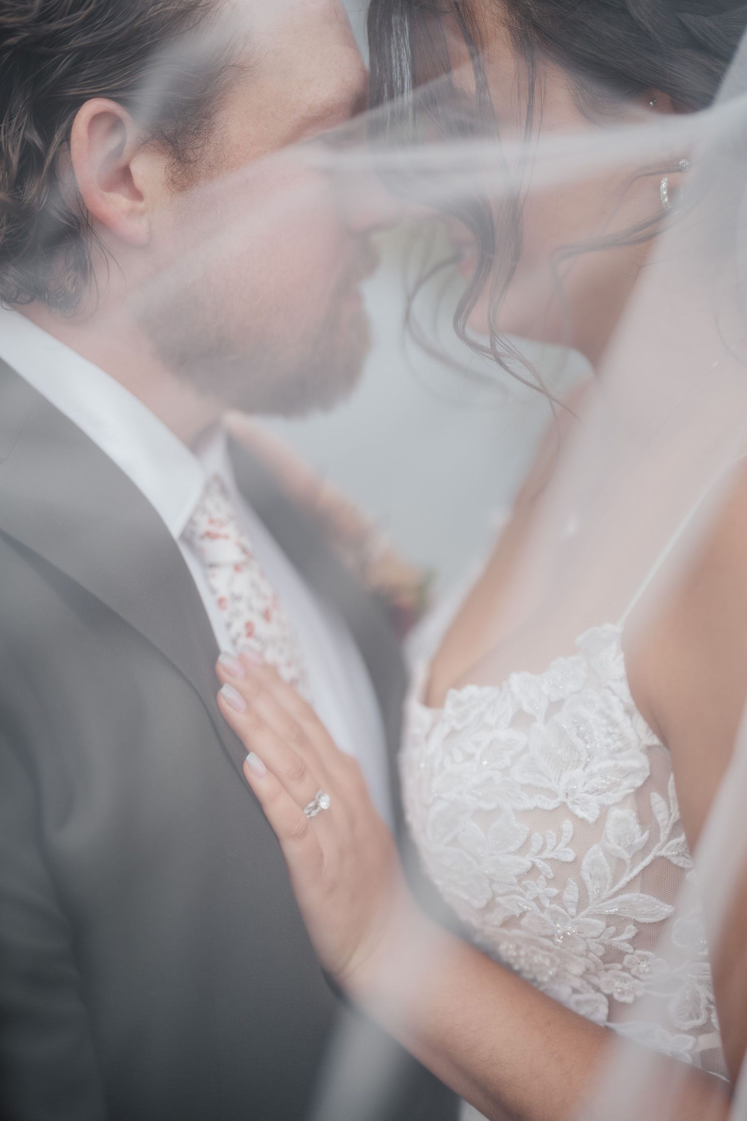 Close-up wedding portrait through delicate veil showing romantic embrace.