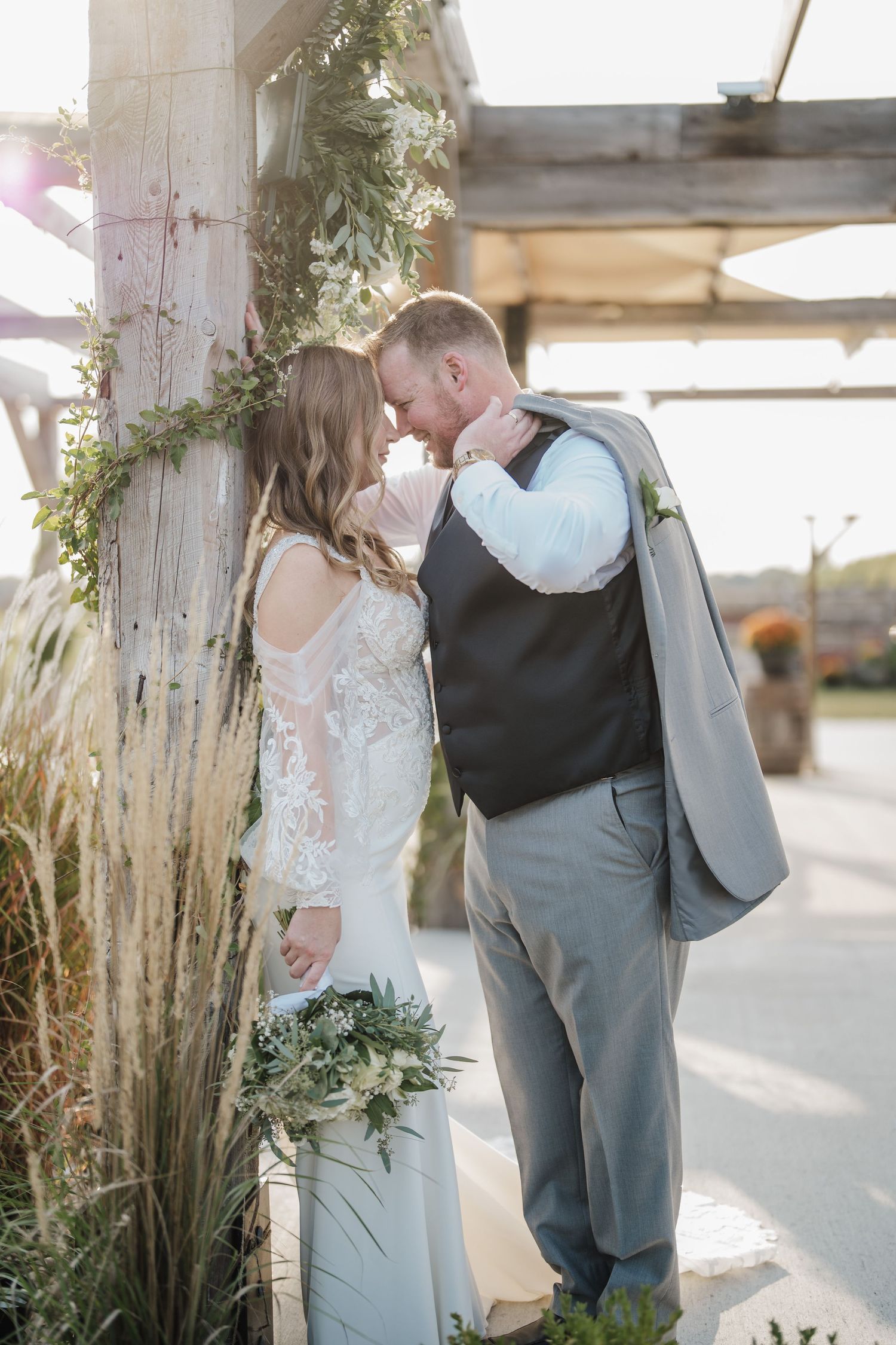 A romantic wedding moment under a decorated pergola with greenery and pampas grass.