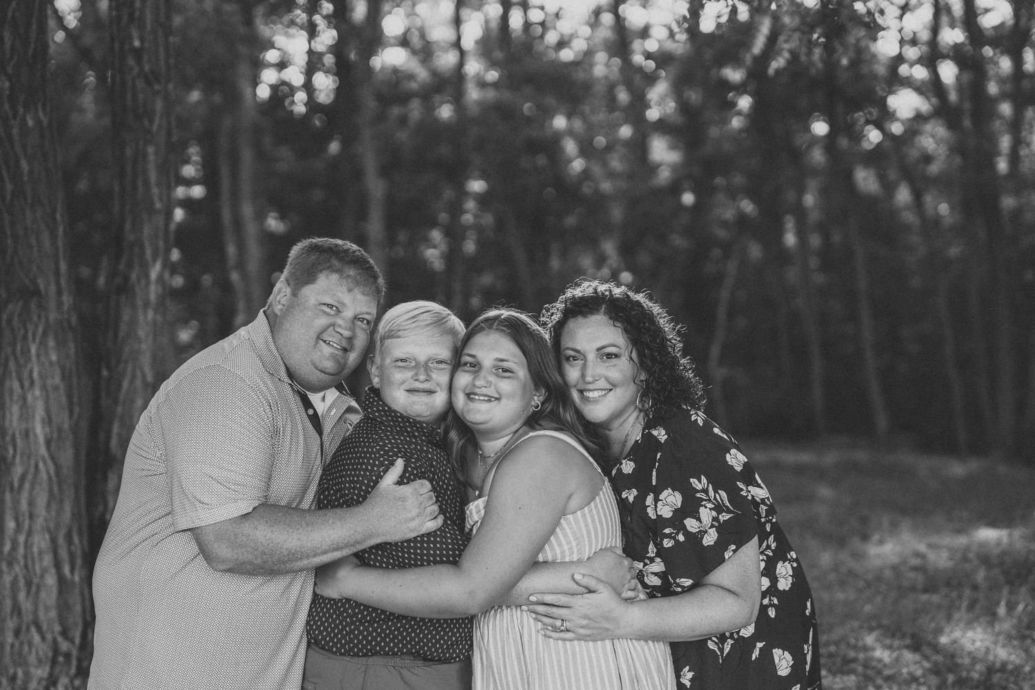 A series of black and white outdoor family portraits showing tender moments and embraces in a natural setting.