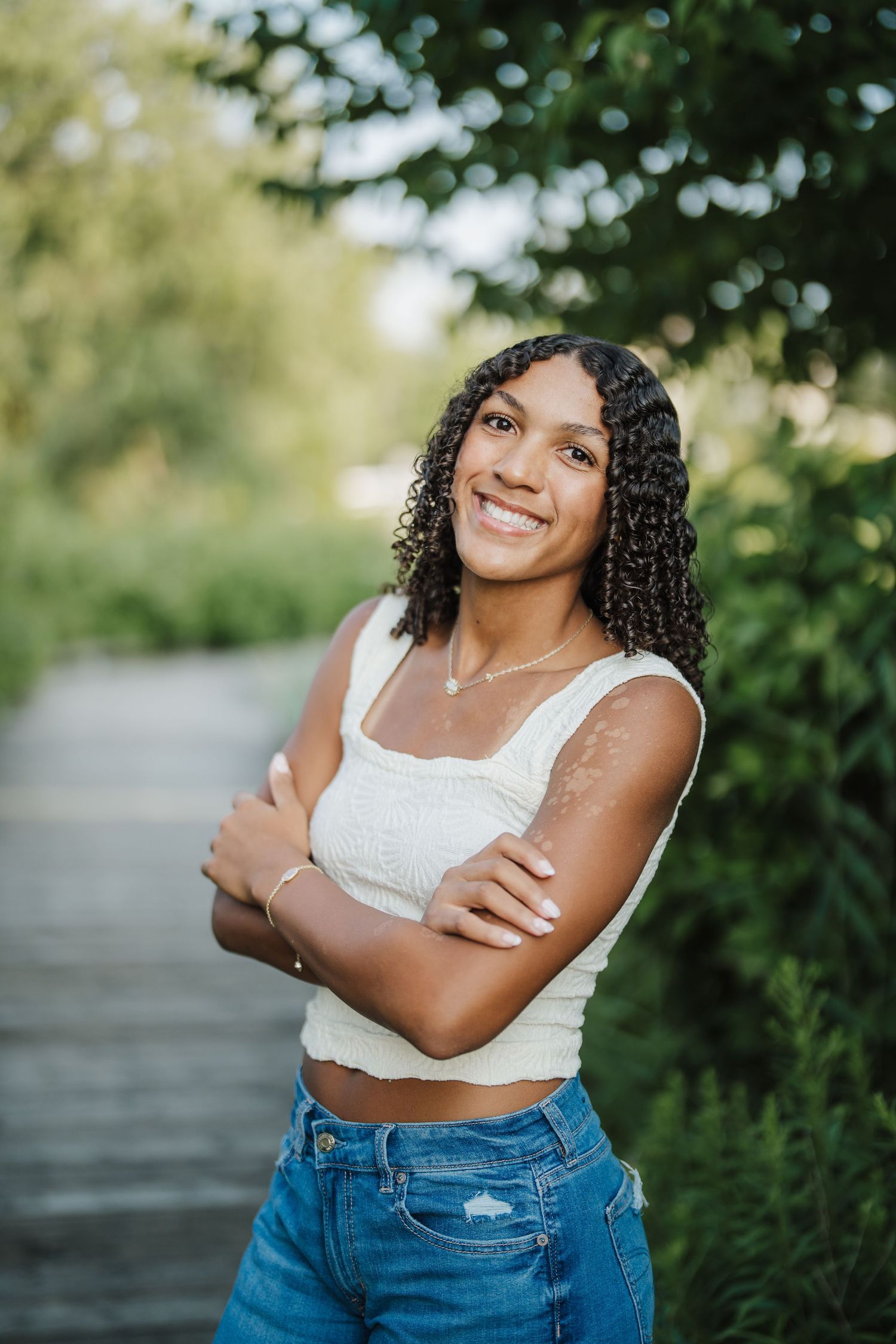 A portrait of someone in a white crop top and distressed jeans posing confidently against a blurred natural background.