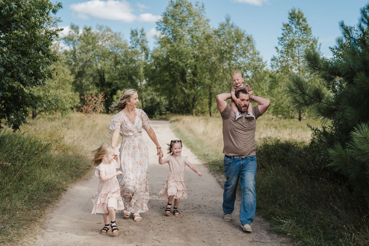 A family walks together on a dirt path surrounded by green trees and grass on a sunny summer day.