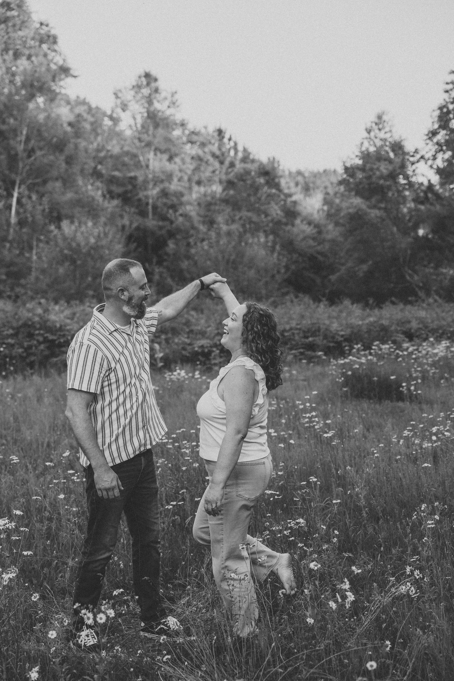 Black and white photo of a couple dancing in a wildflower meadow, man spinning woman under his hand.