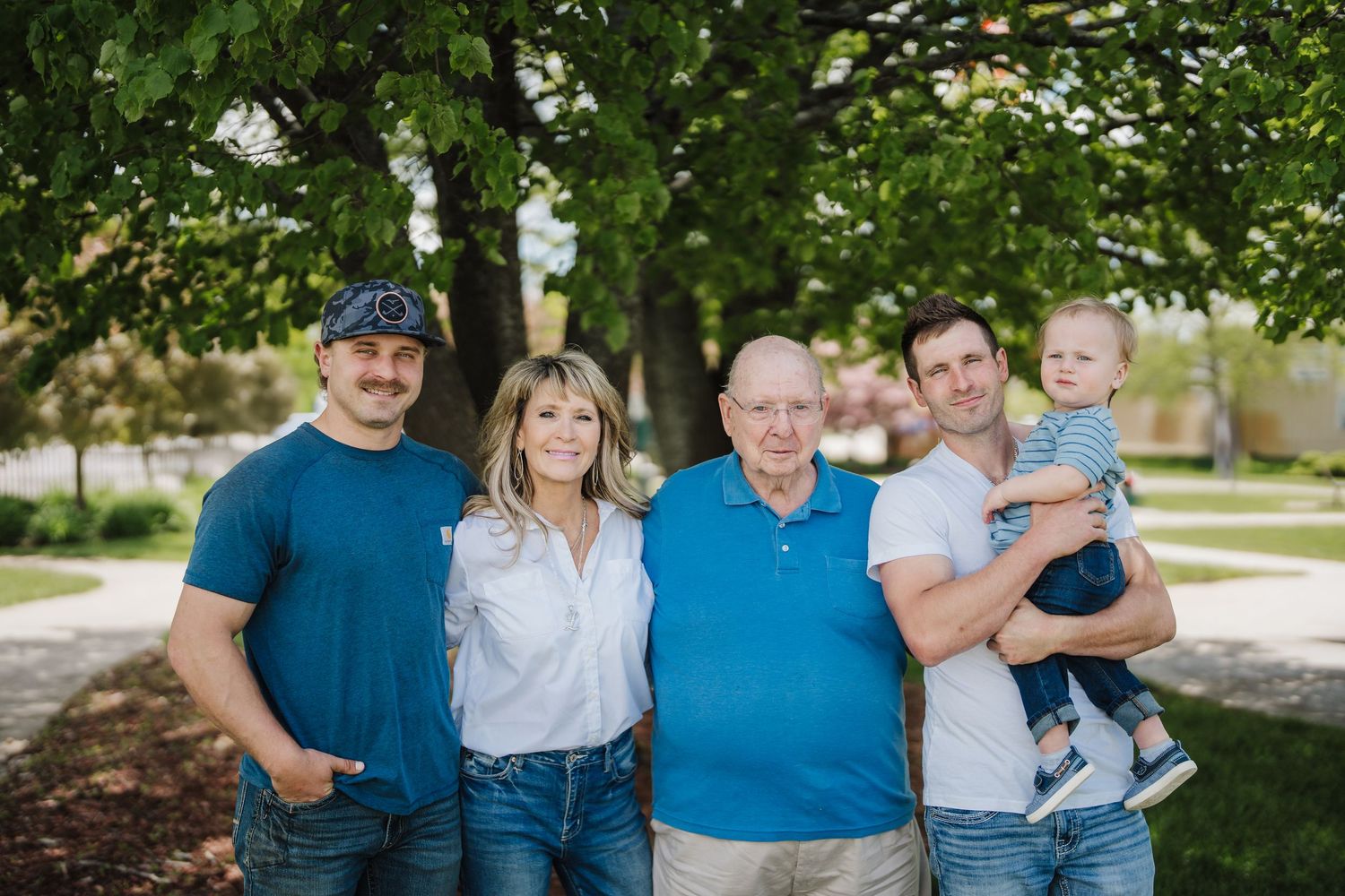 A family wearing coordinated blue and white outfits poses together outdoors in a park setting.