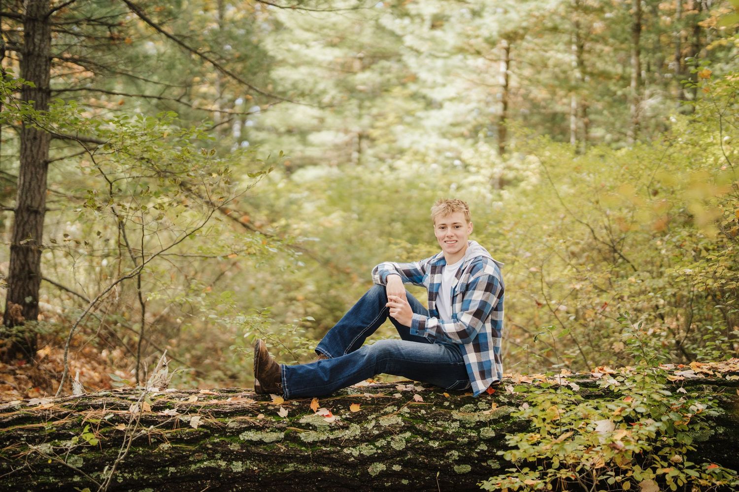 A person in casual attire sits casually on fallen logs in a serene autumn forest setting.