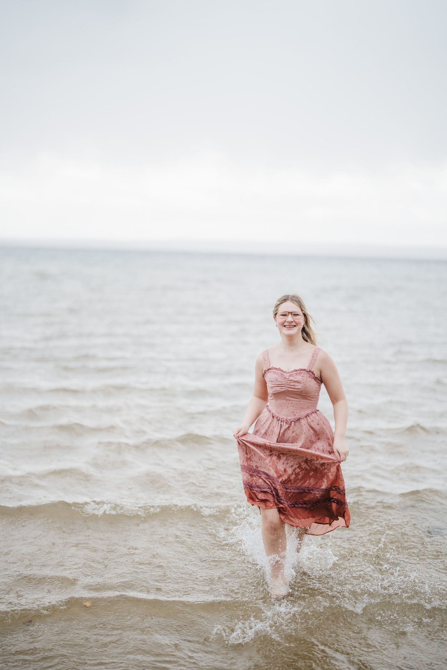 A person in a pink dress splashes and plays in shallow ocean waves at the beach.