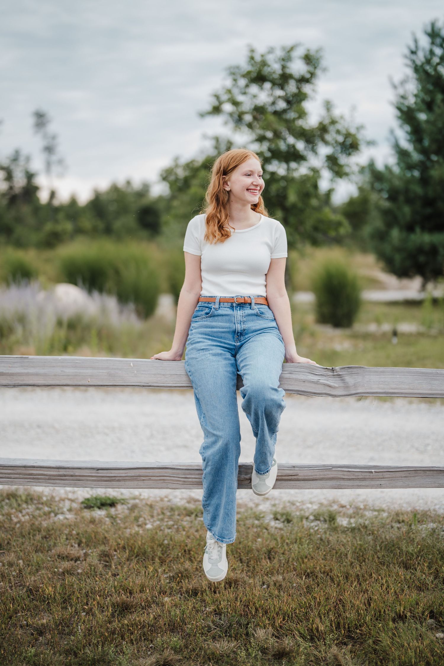 Person in casual summer outfit with white top and blue jeans sits on concrete wall in outdoor garden setting.