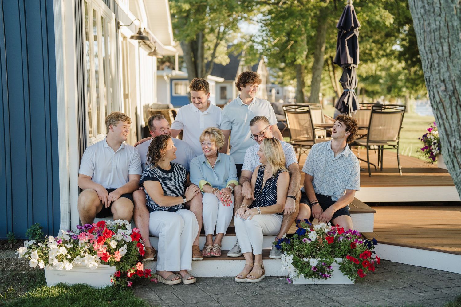 Wedding party sits together on outdoor patio steps with pink floral arrangements and white decor.