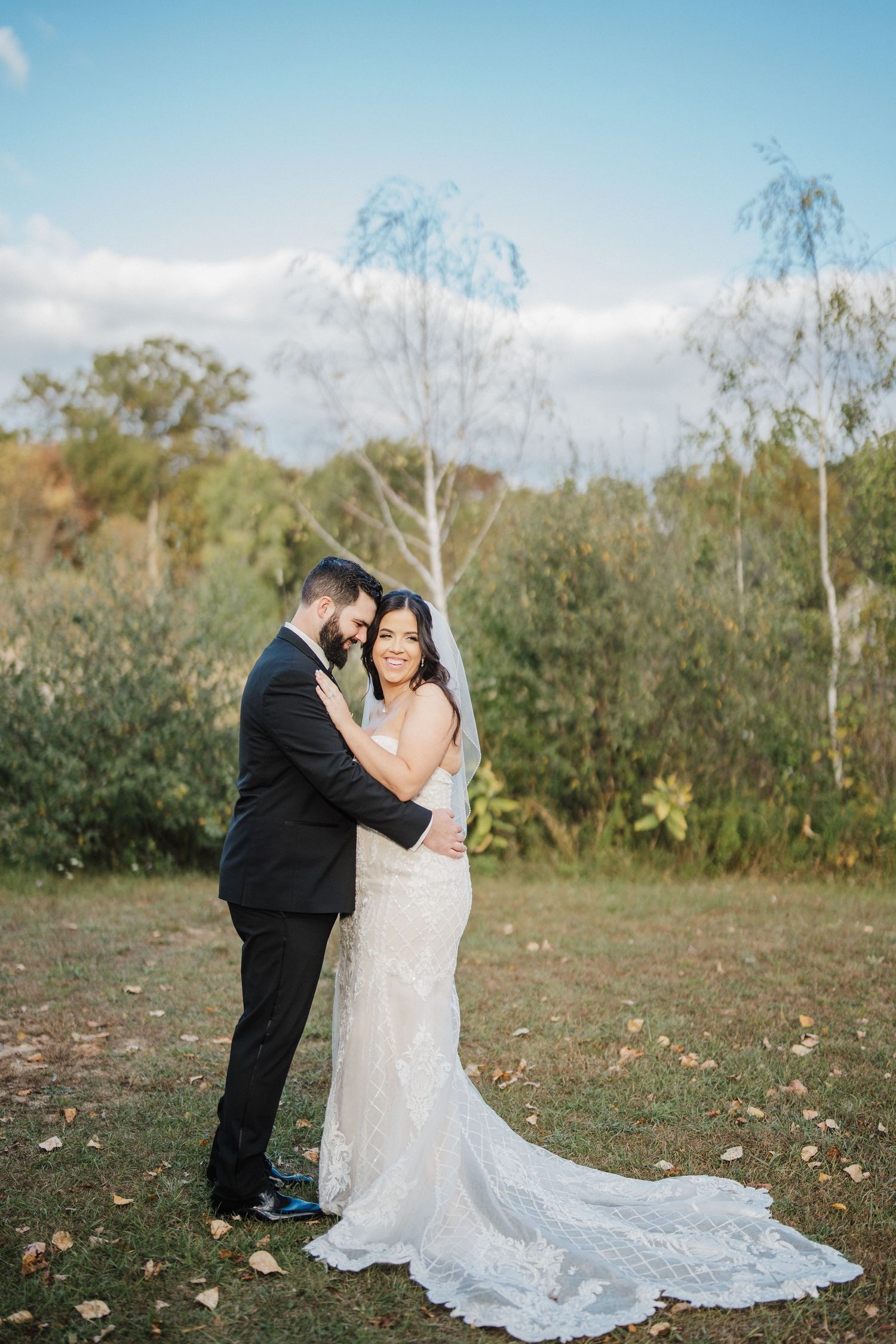 A romantic outdoor wedding photo session in a natural setting with autumn trees and a flowing white lace dress.