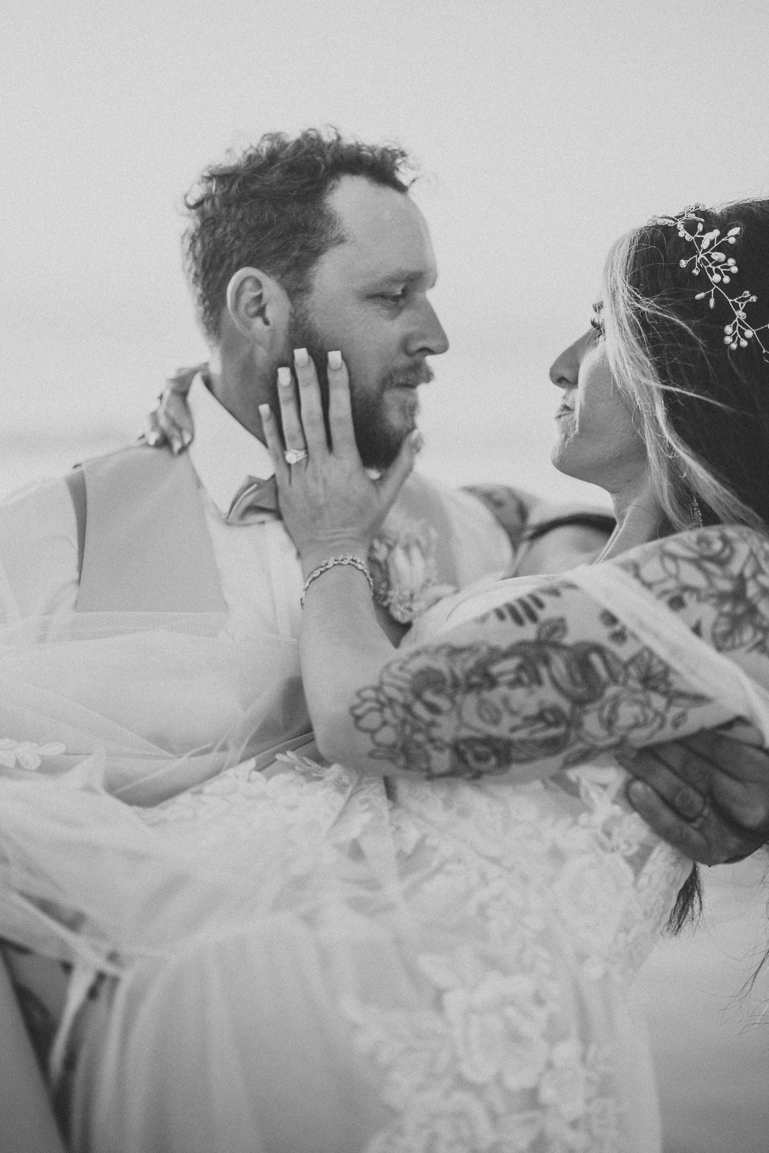 A tender black and white wedding portrait of a couple in an intimate pose, with the bride in lace and groom in a vest.