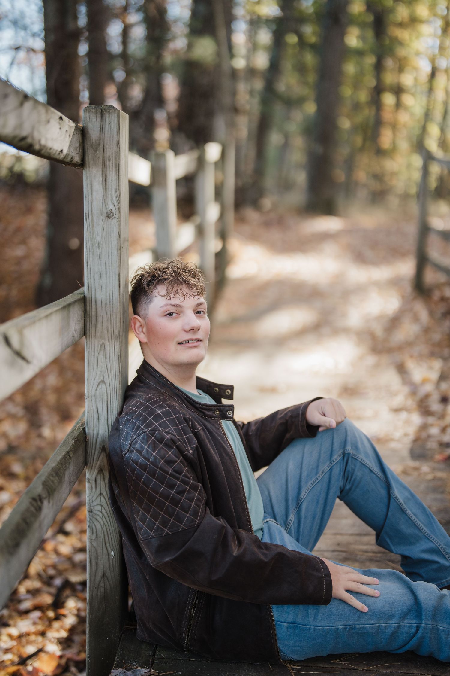 A person relaxes on a wooden deck railing surrounded by autumn leaves and trees in a peaceful forest setting.