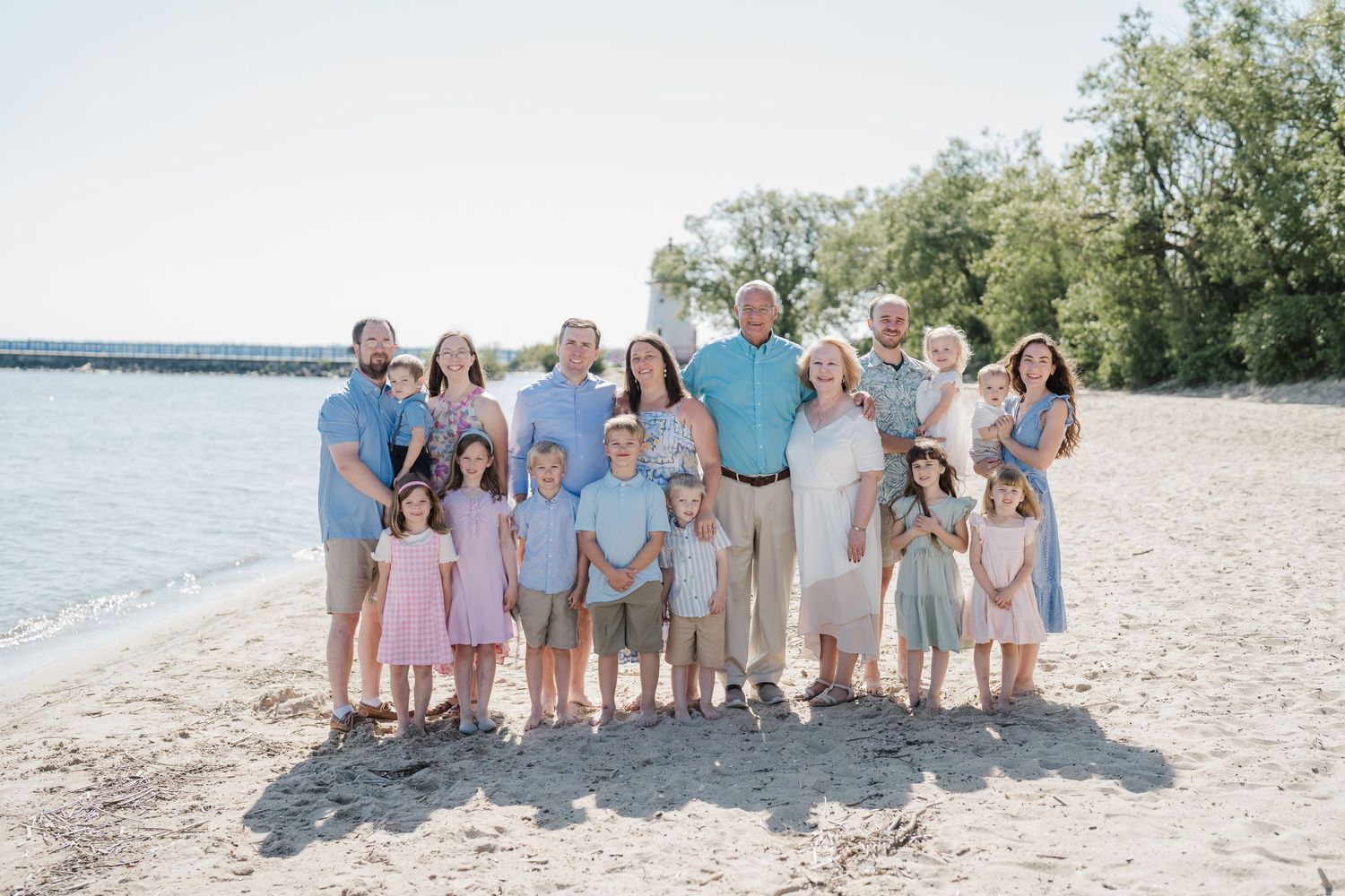 Family members in matching light-colored clothing gather for portraits on a sandy beach.