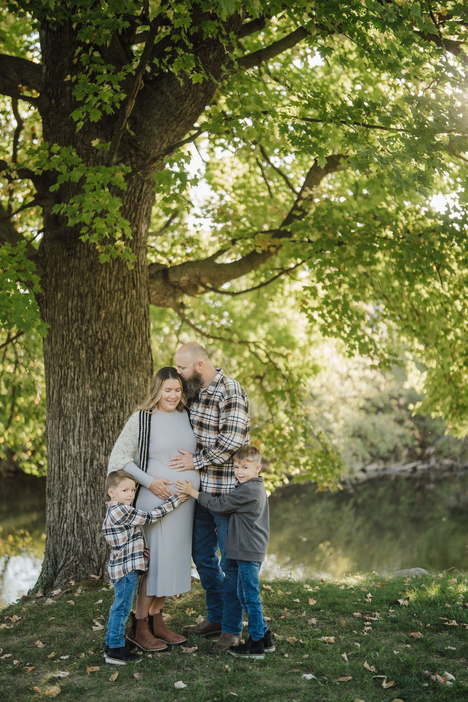 A couple shares tender moments under a large tree during an outdoor maternity photo session in autumn.