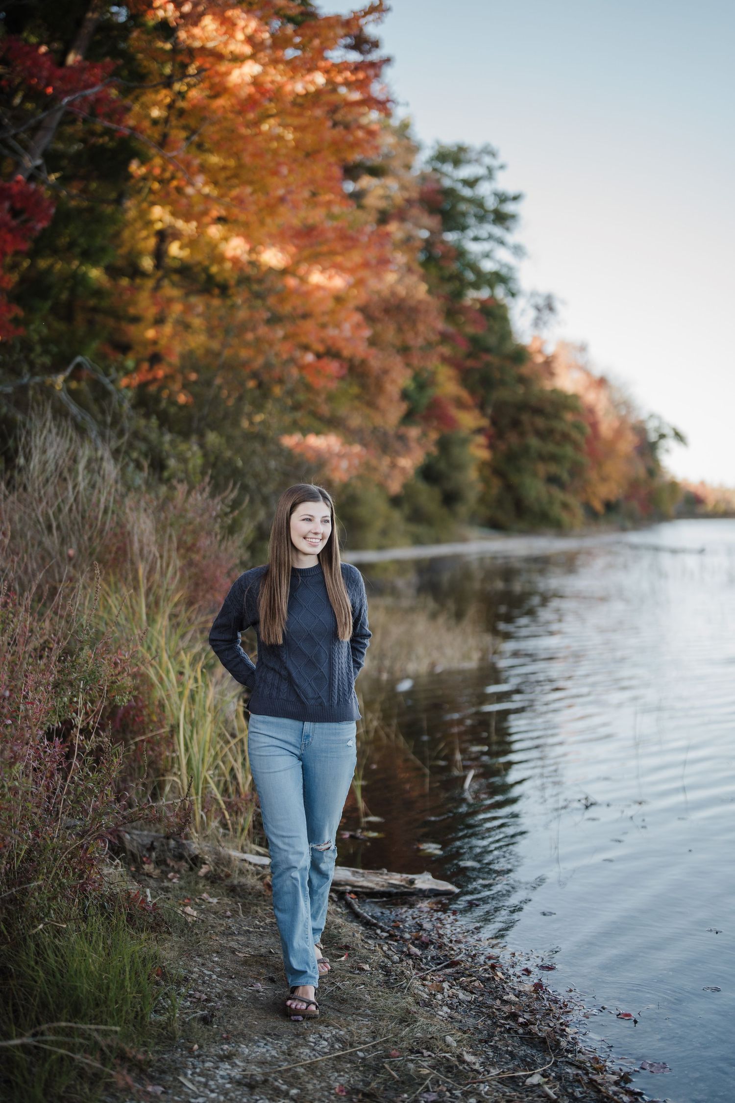 A person walks along a lakeside path during autumn with colorful fall foliage reflecting in the water.